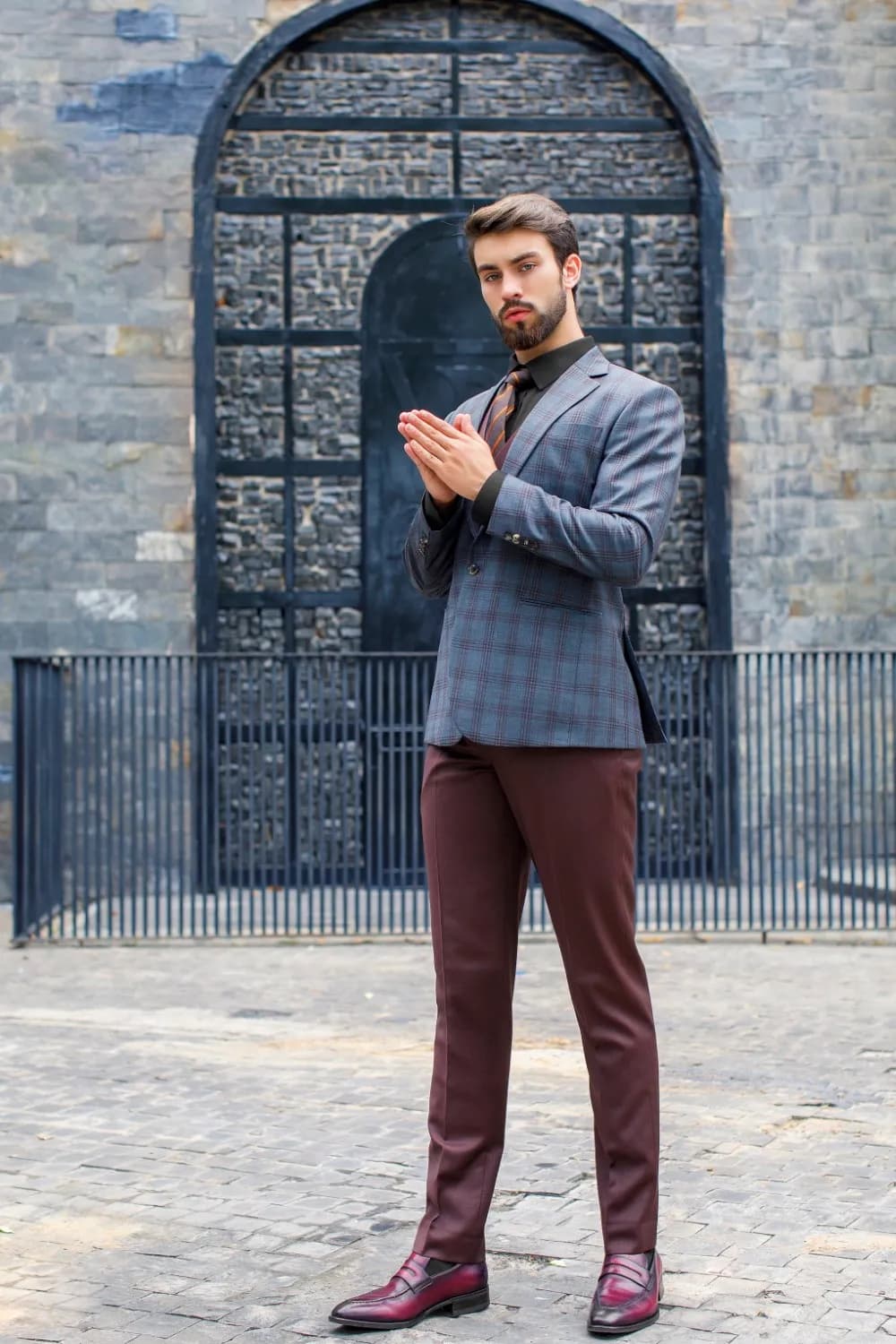 Blazer xanh xám caro, quần đỏ rượu, giày lười, dáng đứng trước cổng sắt