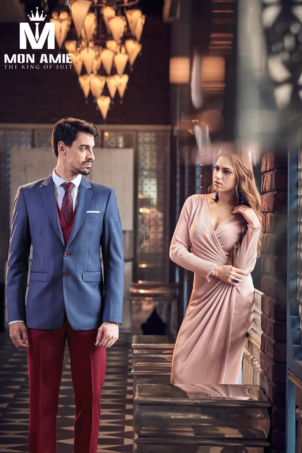 Suit xanh hoàng gia quần đỏ rượu, cạnh cô gái váy hồng, nền đèn chùm