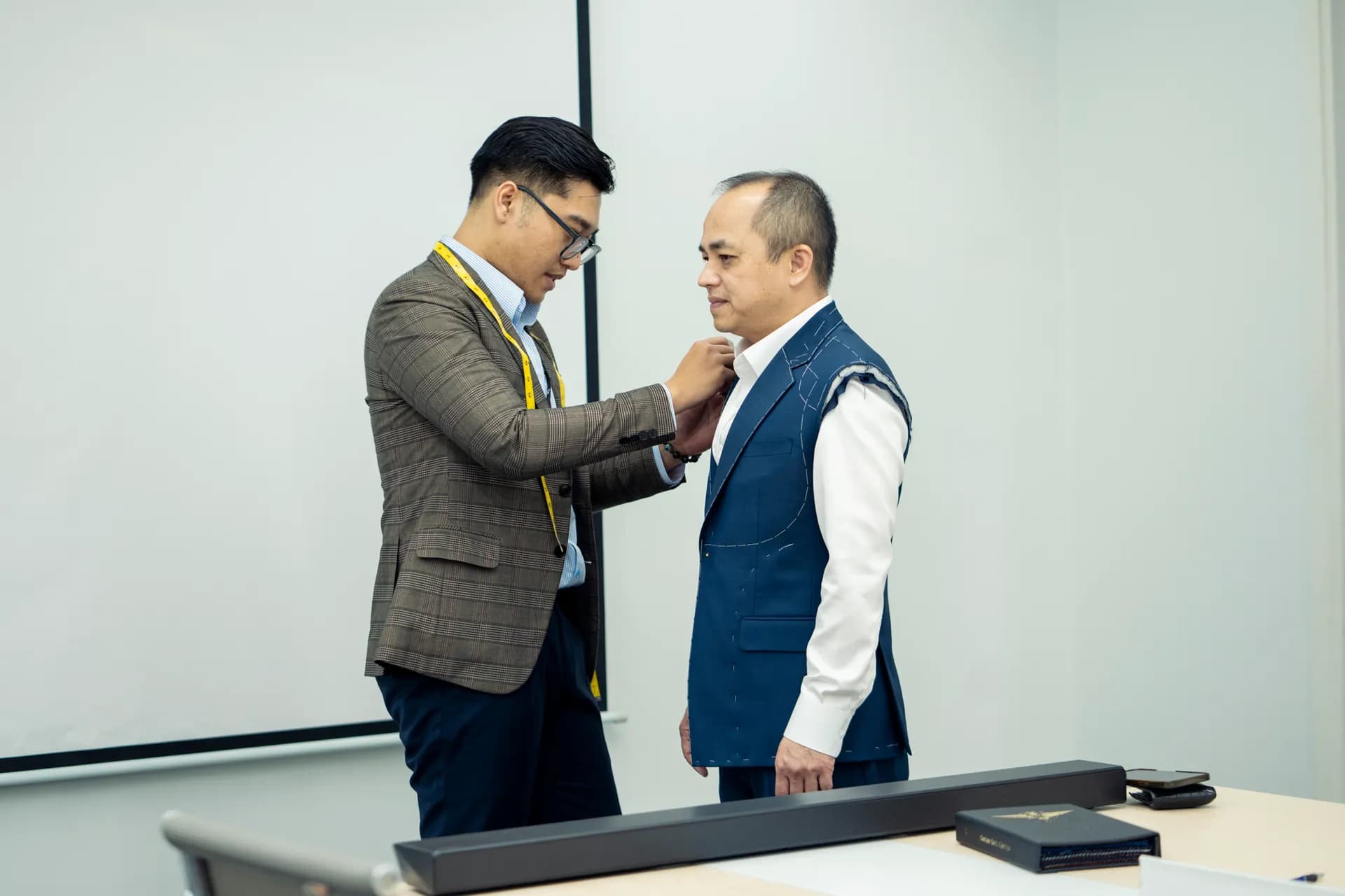 Thợ may chỉnh cổ áo vest xanh còn lược chỉ cho khách trong buổi thử đồ