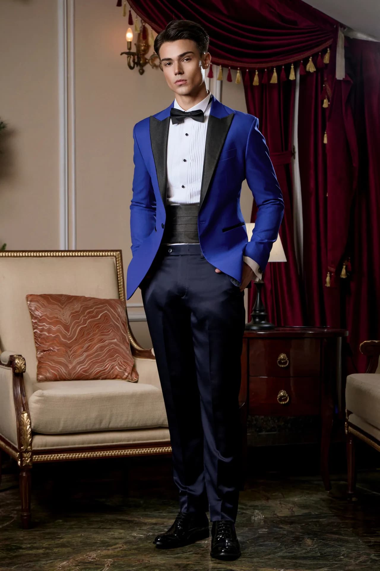 Tuxedo xanh royal ve đen, đai bụng đen, đứng toàn thân bên ghế bành cổ điển