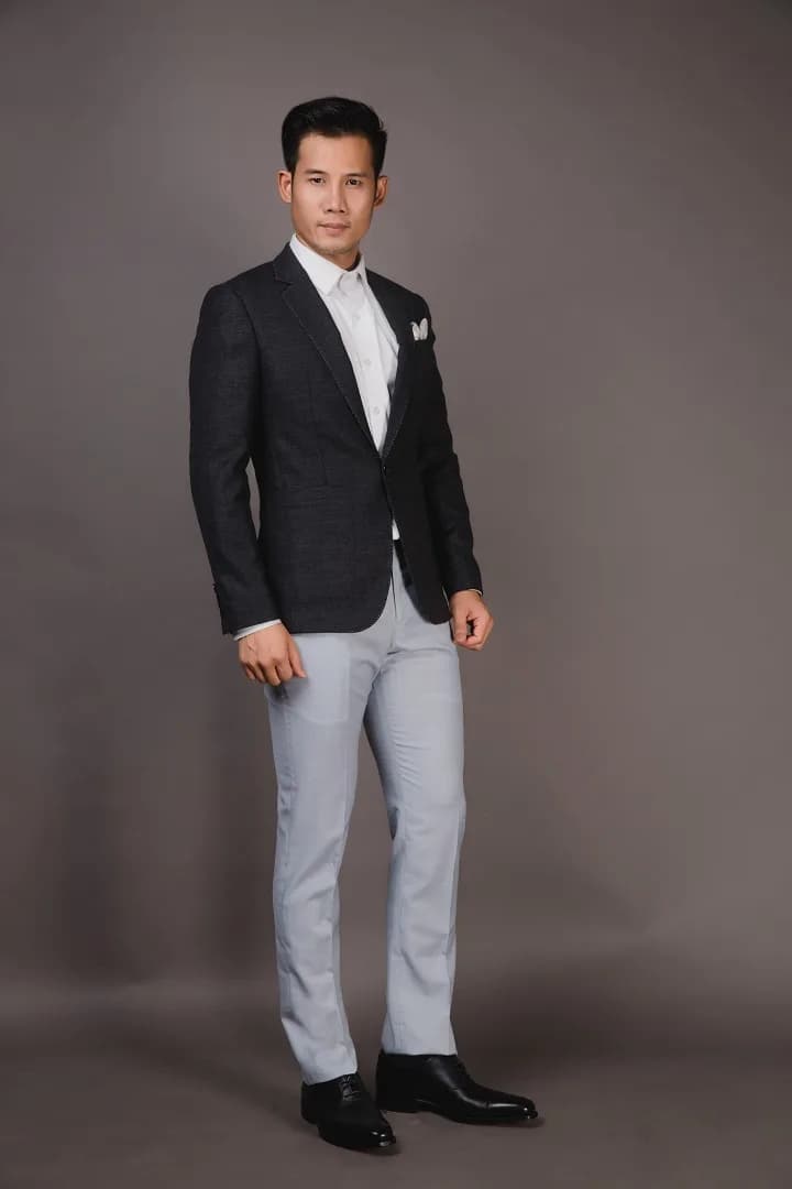Tuxedo đen ve lụa, nơ cổ, dáng đứng khoanh tay giữa hàng cột gỗ chạm