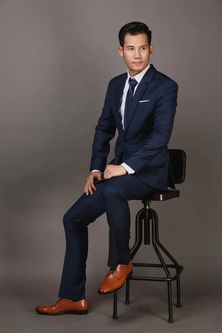Suit xanh navy ngồi trên ghế sắt, giày da nâu, nền studio