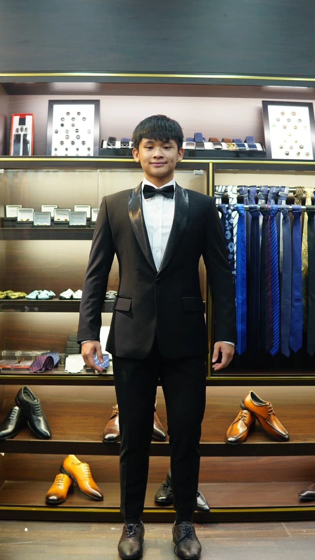 Khách mặc tuxedo đen cổ ve satin, nơ đen, giữa kệ giày showroom
