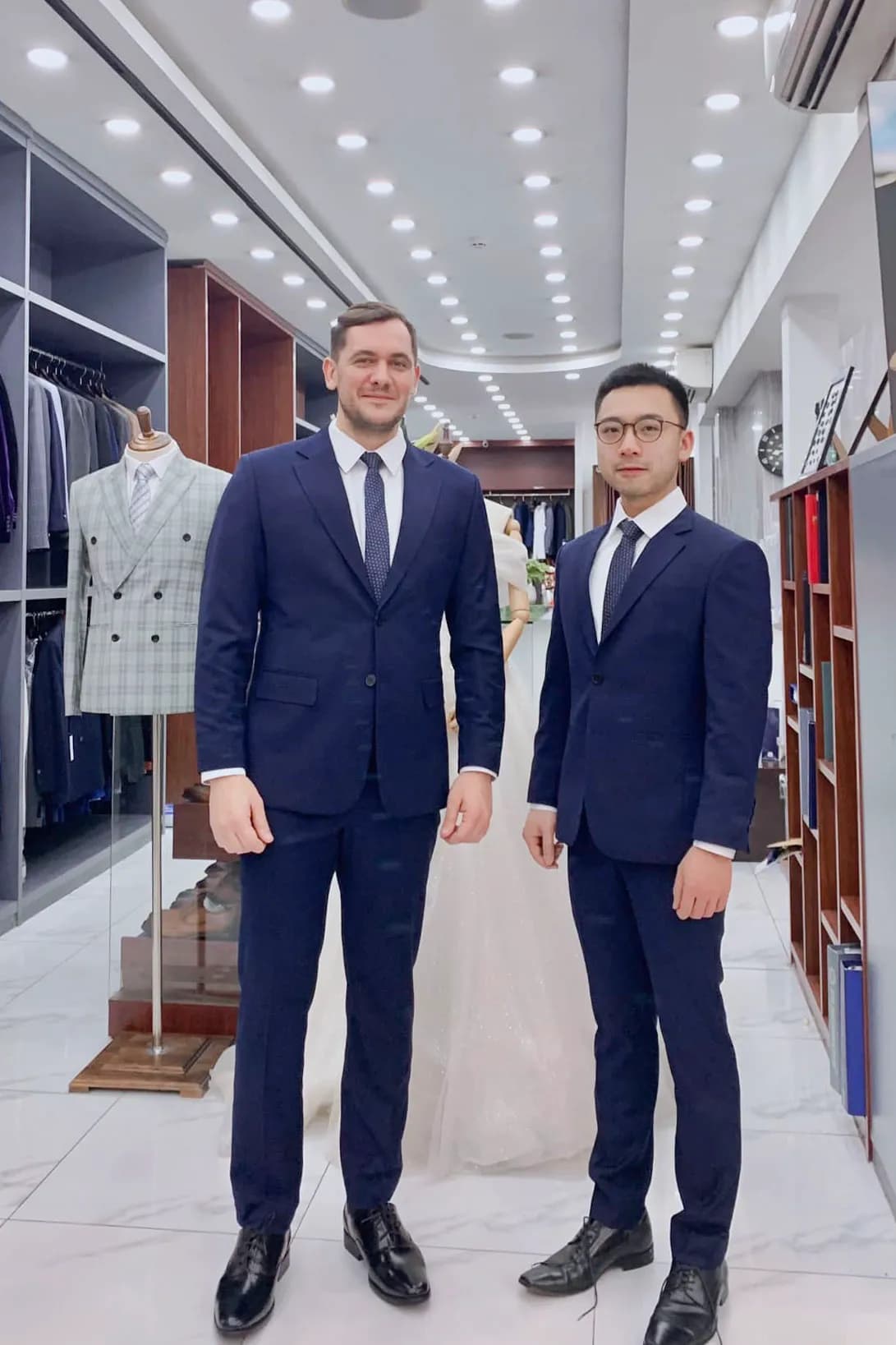 Hai khách mặc suit navy chụp chung trong showroom