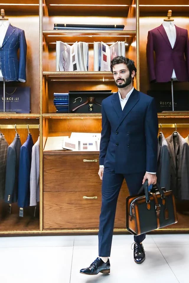 Khách mặc suit hai hàng navy cầm cặp da, bước đi tại showroom