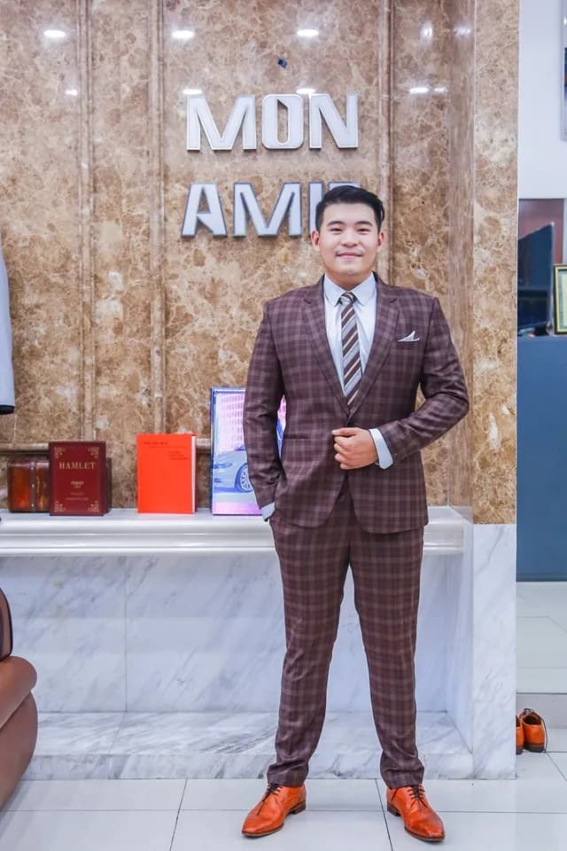 Khách mặc suit ca-rô đỏ đô ba mảnh, trước logo Mon Amie