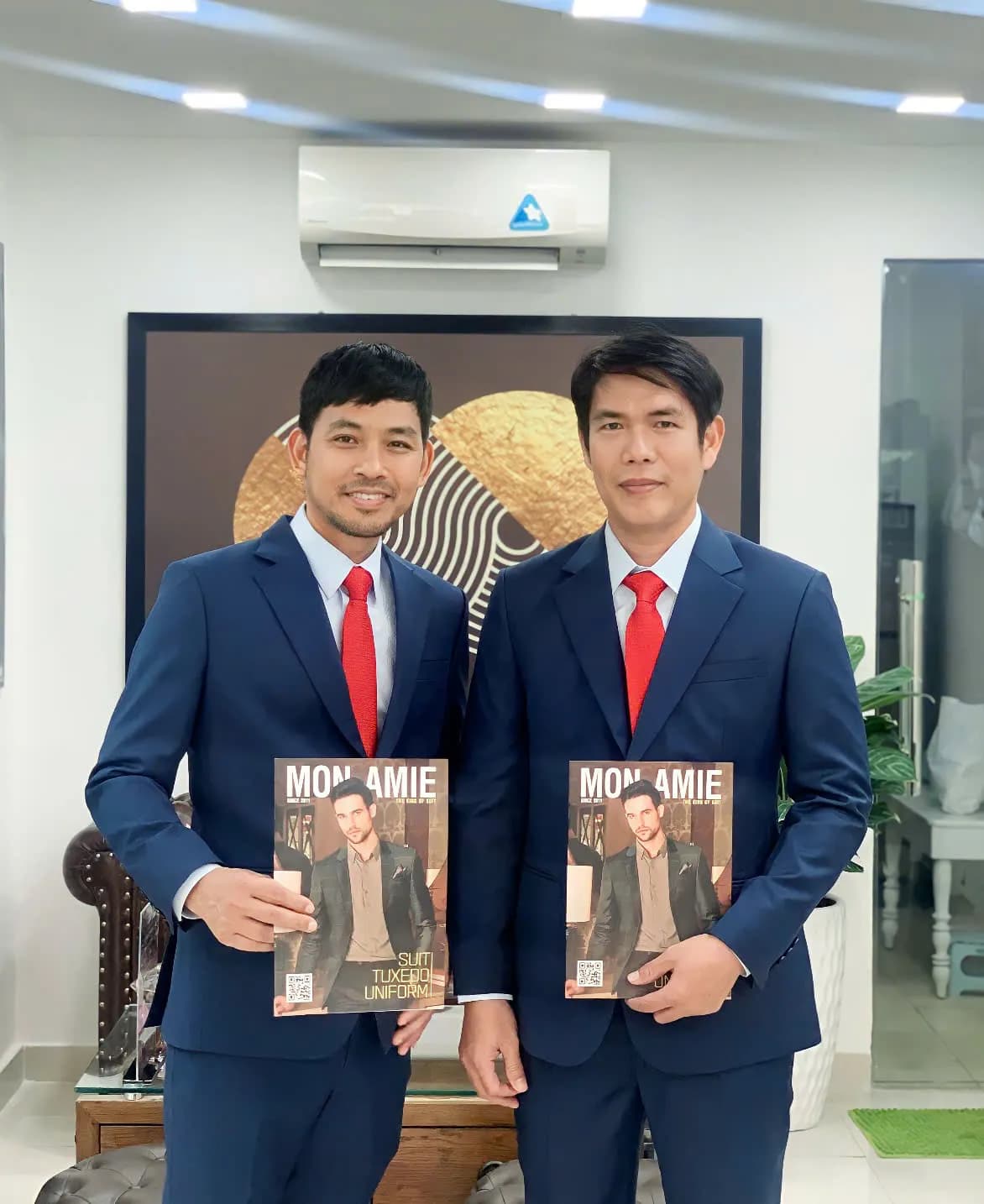 Hai khách mặc suit navy cà vạt đỏ, cầm tạp chí Mon Amie tại showroom
