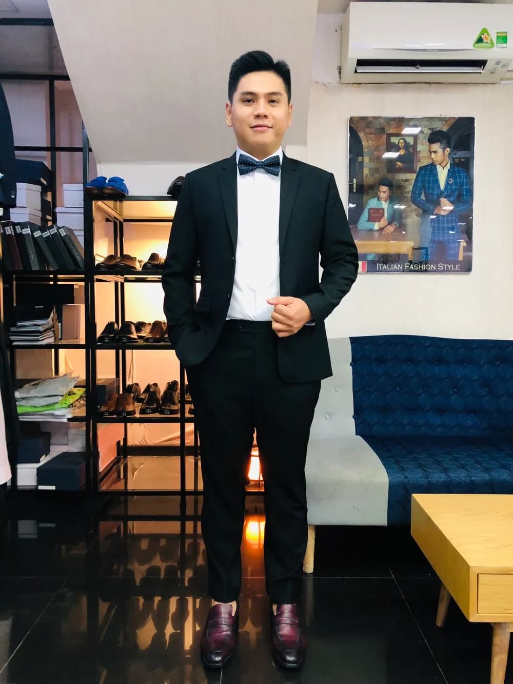 Khách mặc tuxedo đen nơ đen, giày da bóng, tự tin trong showroom