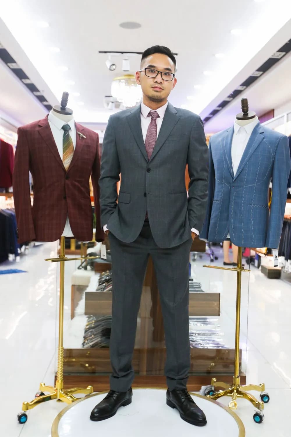 Khách mặc suit xám cà vạt đỏ đô, đứng giữa hai mannequin