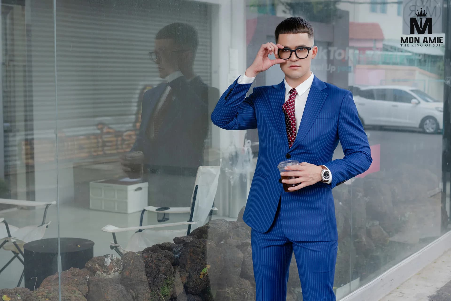 Tuxedo đen cổ ve lụa, nơ đen, dáng khoanh tay bên cột gỗ chạm