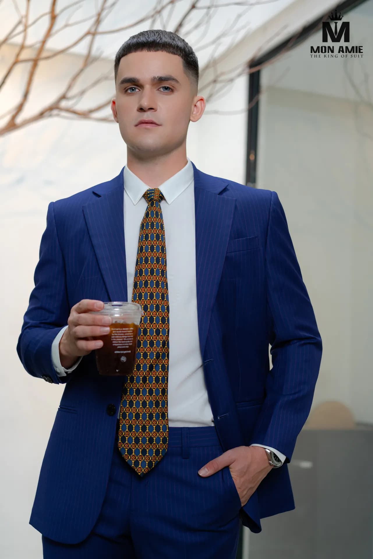 Suit xanh sapphire, cà vạt họa tiết vàng, tay cầm ly cà phê
