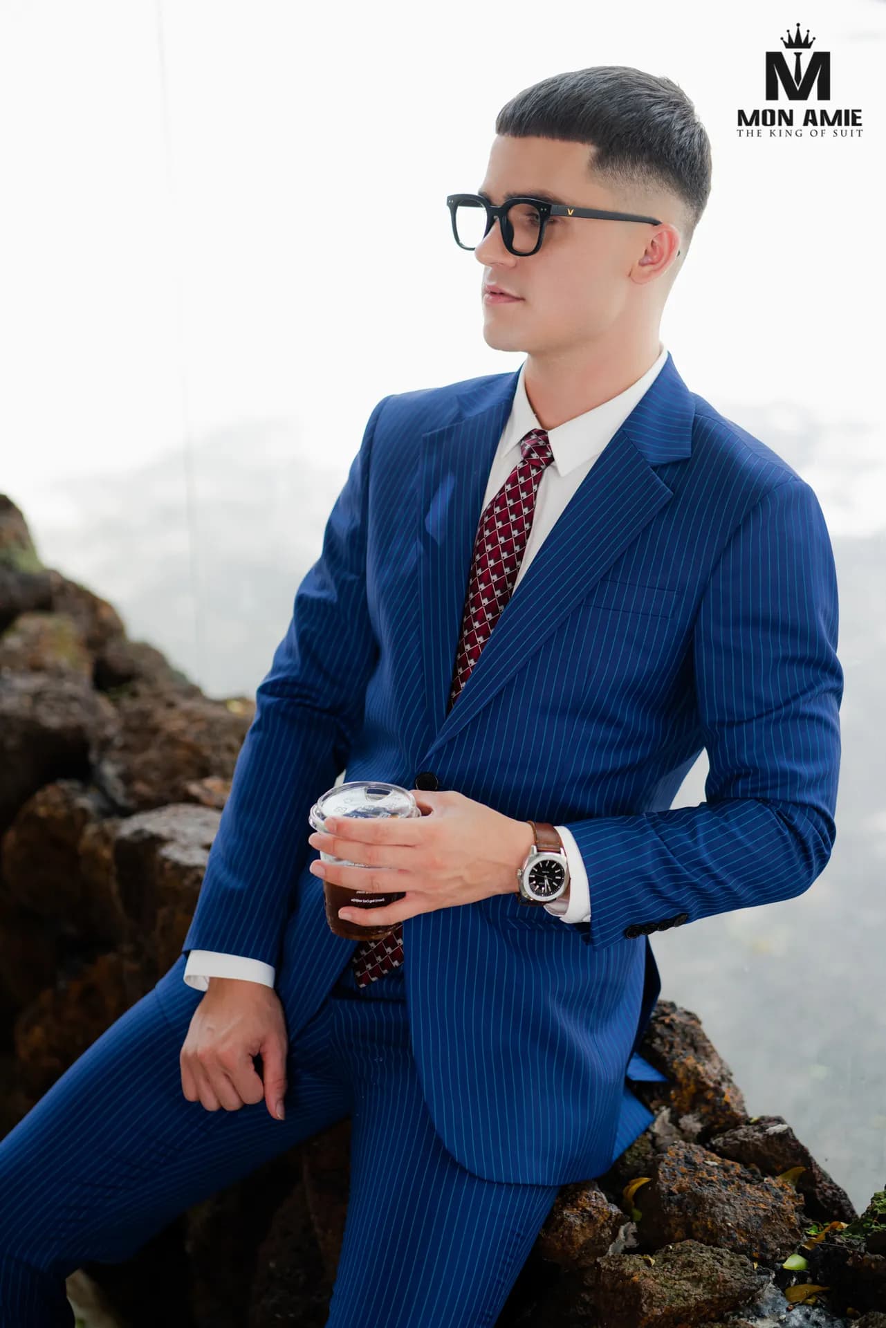 Suit xanh sapphire kẻ sọc, kính đen, ngồi trên đá nhìn nghiêng