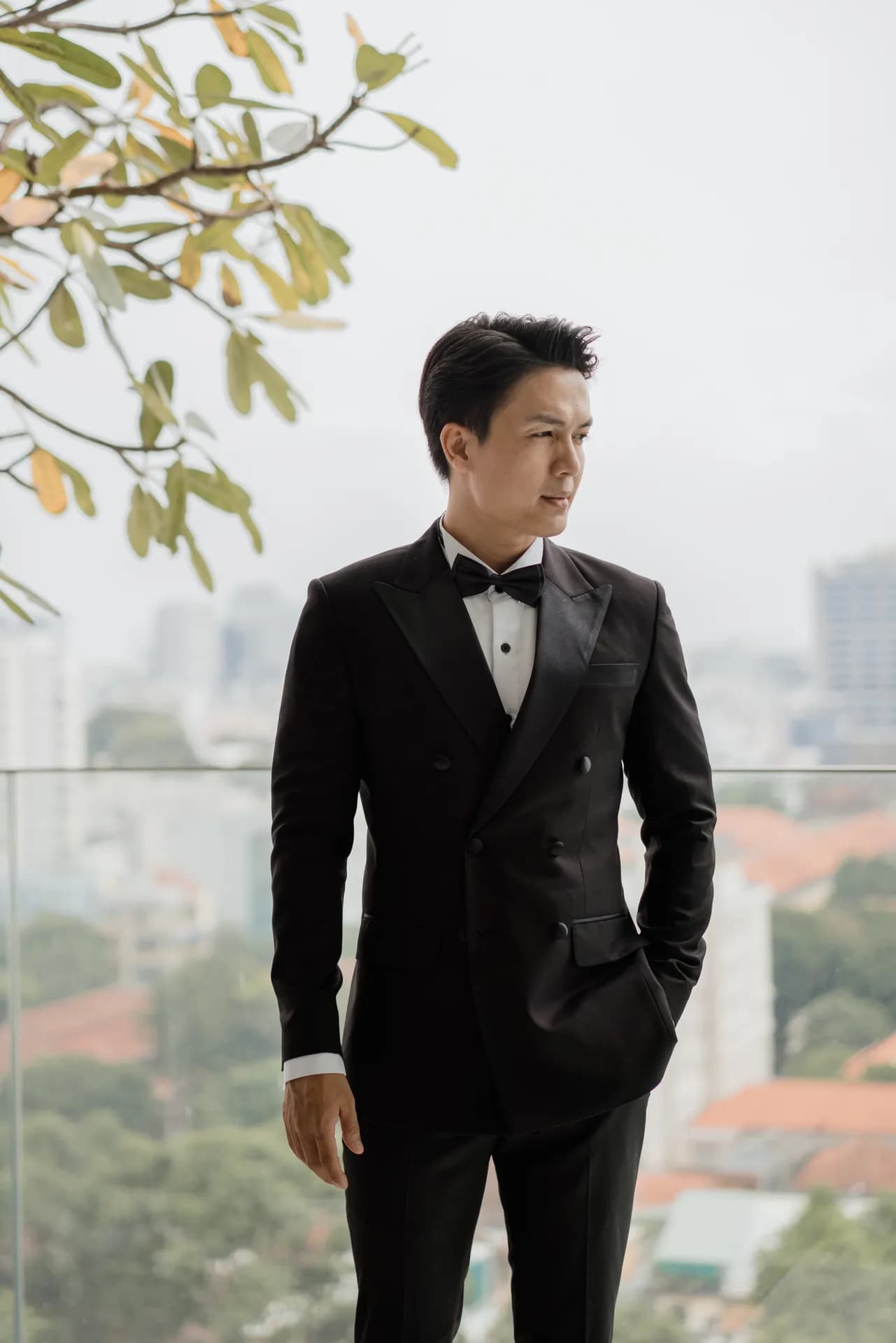 Tuxedo đen nơ đen, đứng ban công nhìn ra thành phố