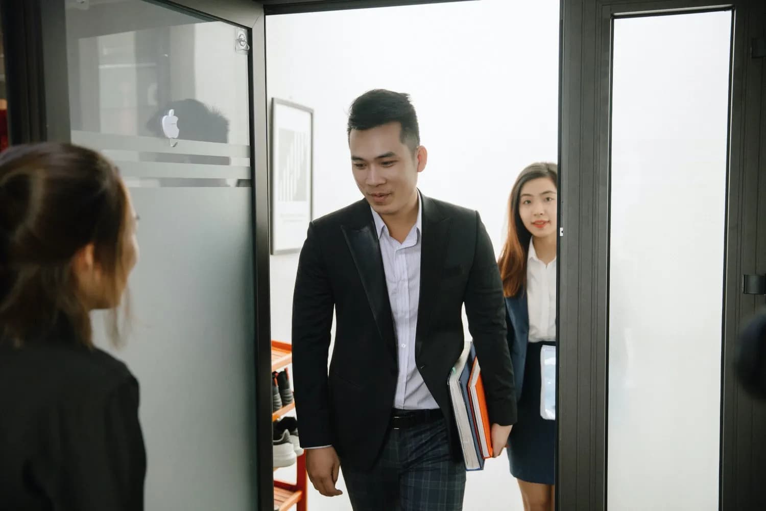 Khách vest đen cổ lụa bước vào văn phòng cùng nữ đồng nghiệp