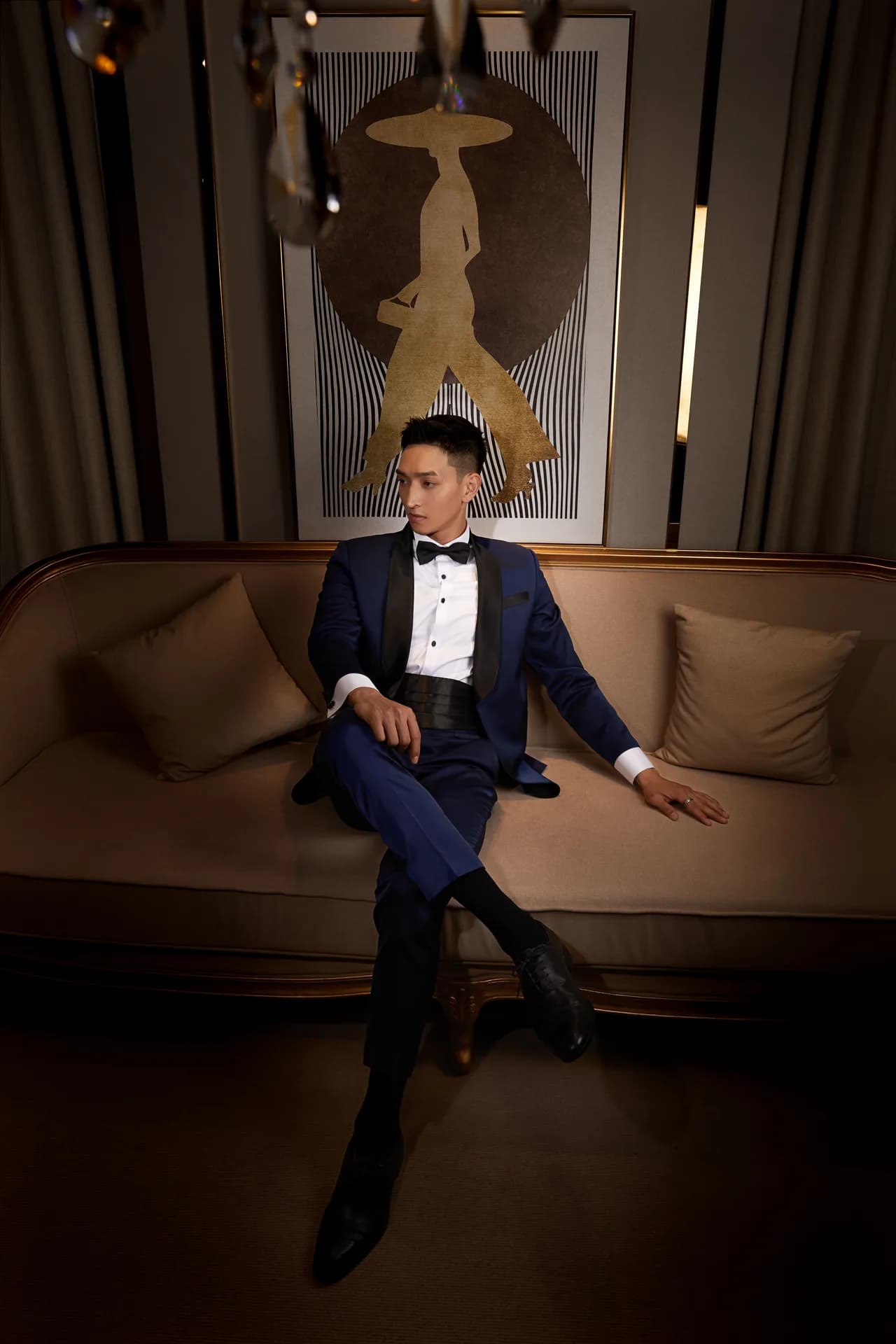 Tuxedo xanh navy ve nhung đen, nơ đen, ngồi vắt chân trên ghế sofa