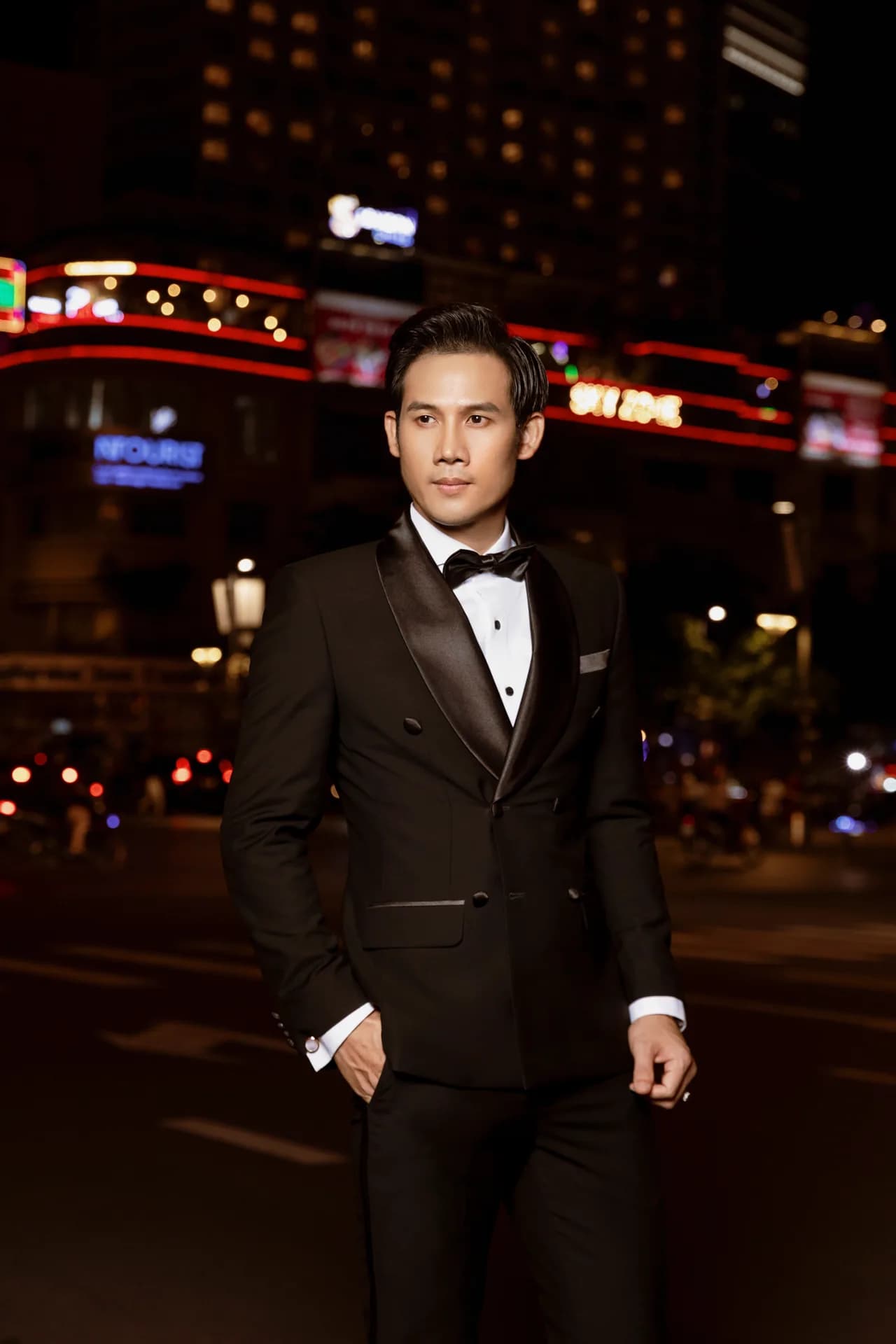 Tuxedo đen hai hàng khuy ve satin, nơ đen, khung phố đèn neon về đêm