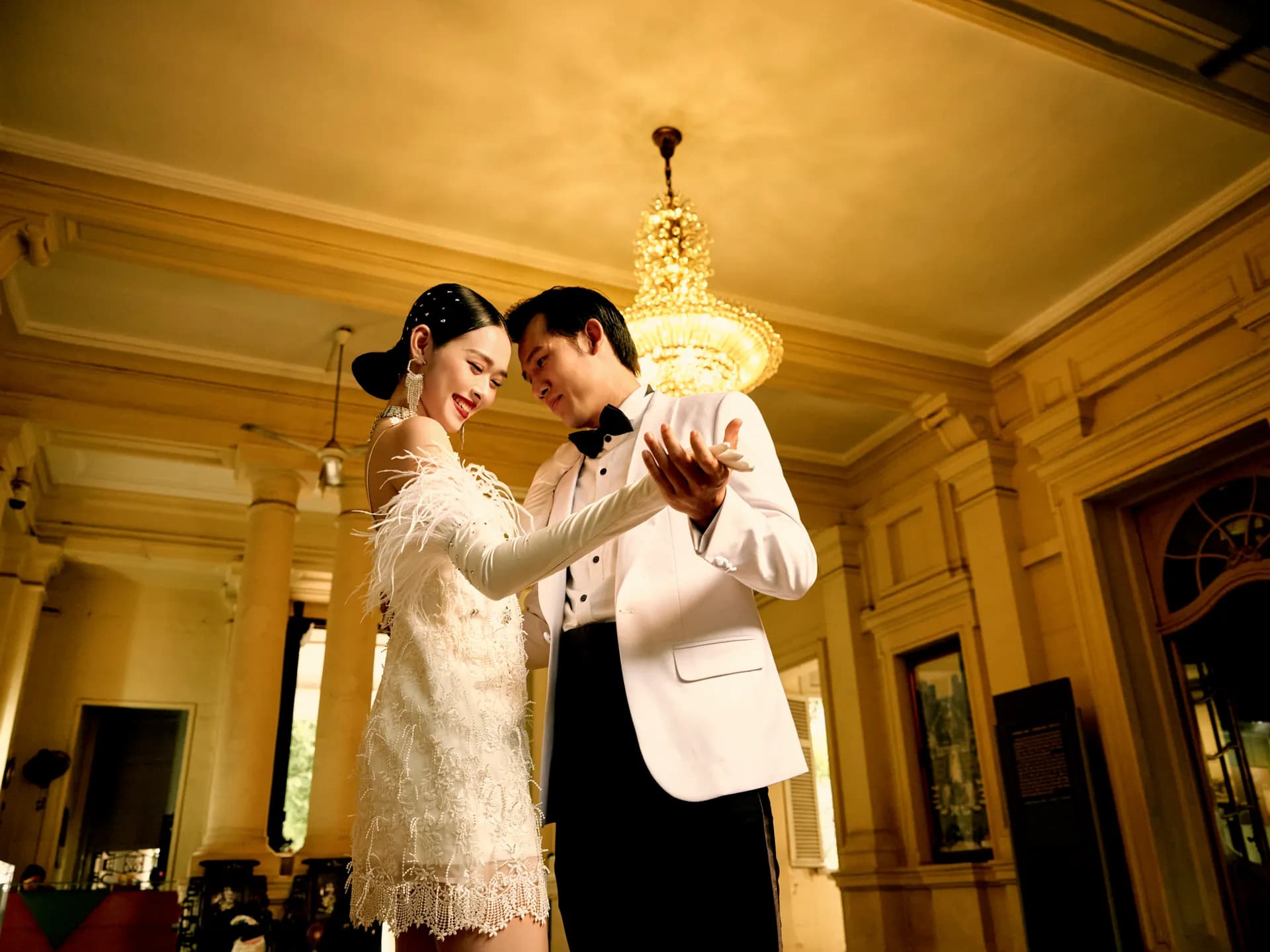 Tuxedo trắng cùng váy ren lông vũ, khiêu vũ dưới đèn chùm cổ điển