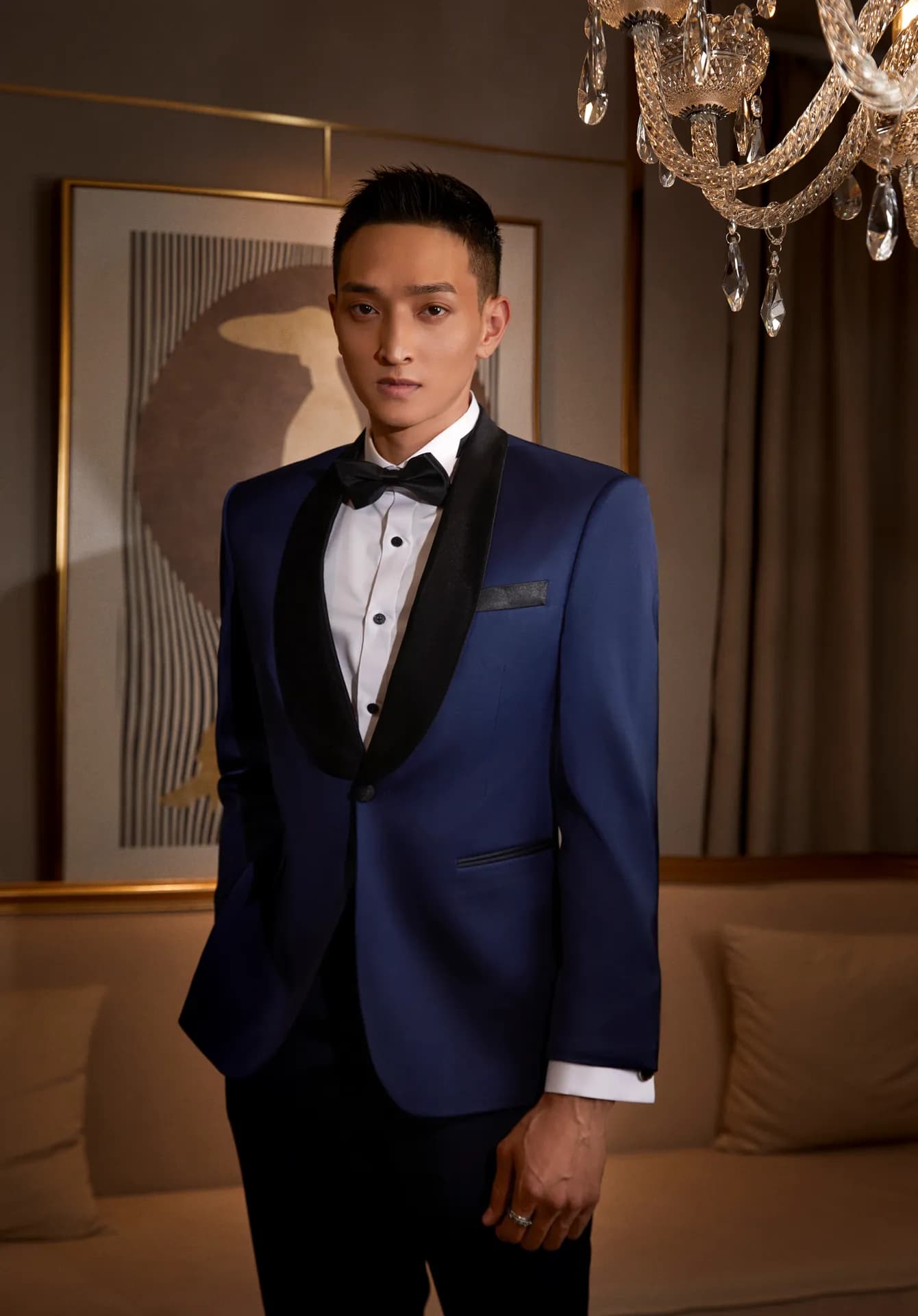Tuxedo xanh sapphire ve nhung đen, nơ đen, đứng trong phòng khách sang trọng