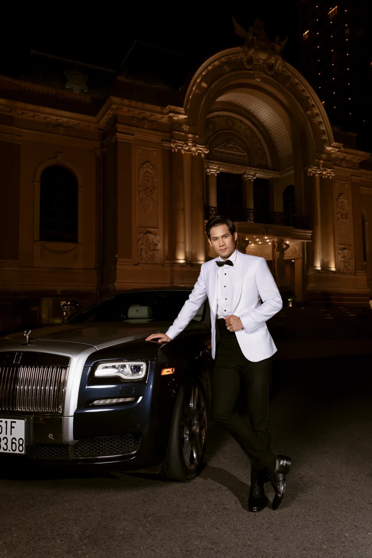 Tuxedo trắng dáng tựa xe sang trước nhà hát cổ về đêm