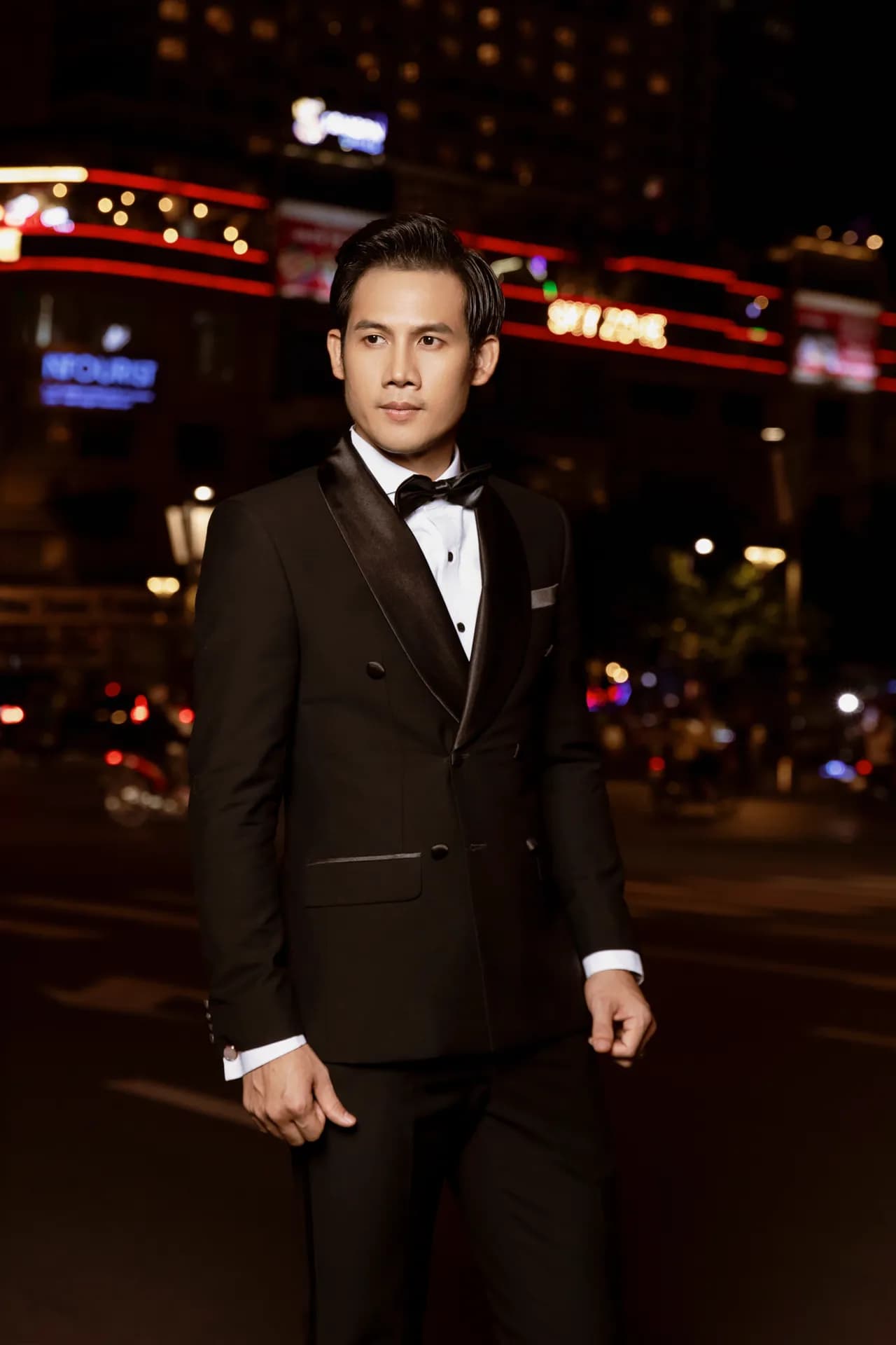 Tuxedo đen cài hai hàng khuy ve satin, đứng giữa phố đêm đèn neon