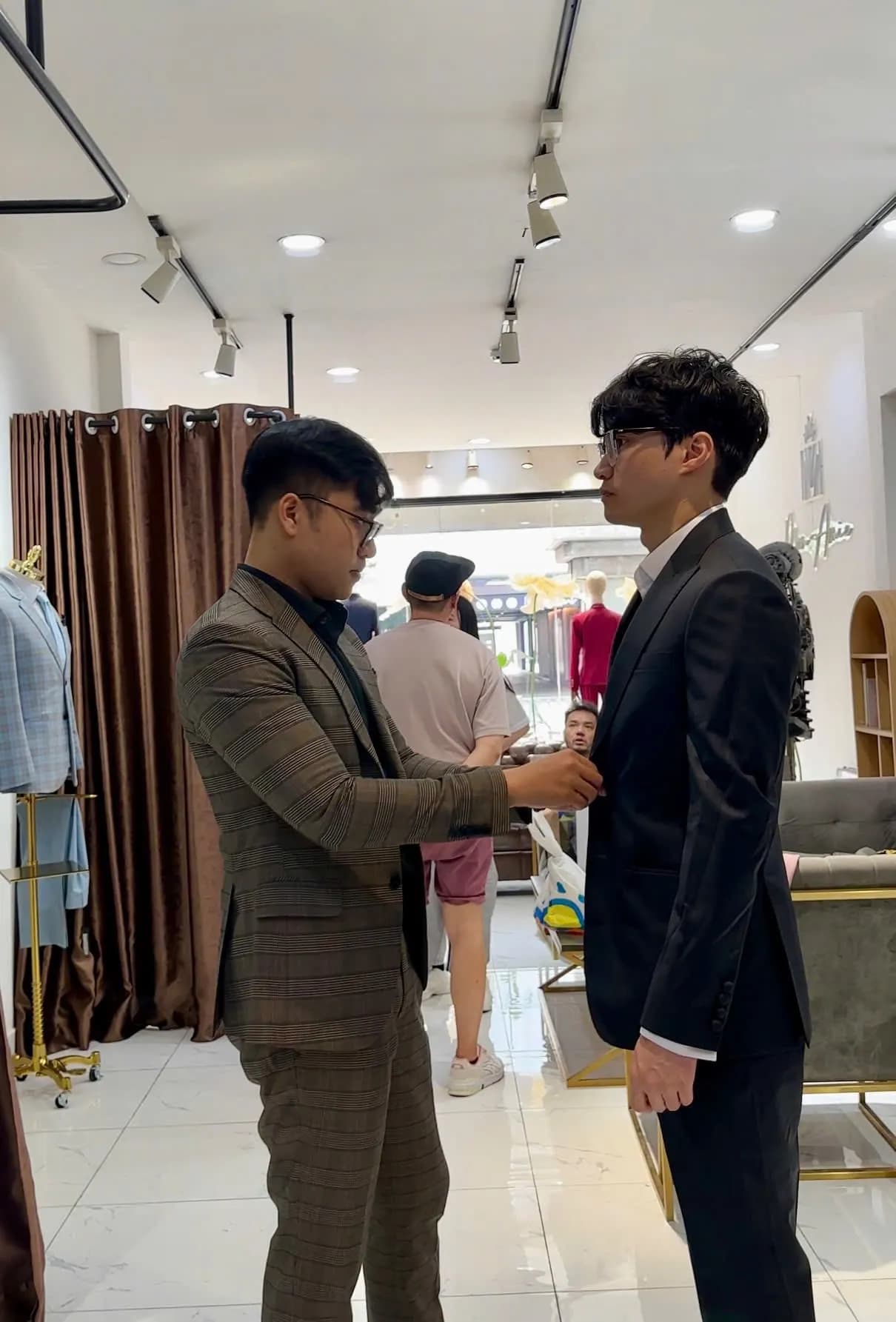Thợ may chỉnh vai áo vest đen cho khách thử đồ trong showroom