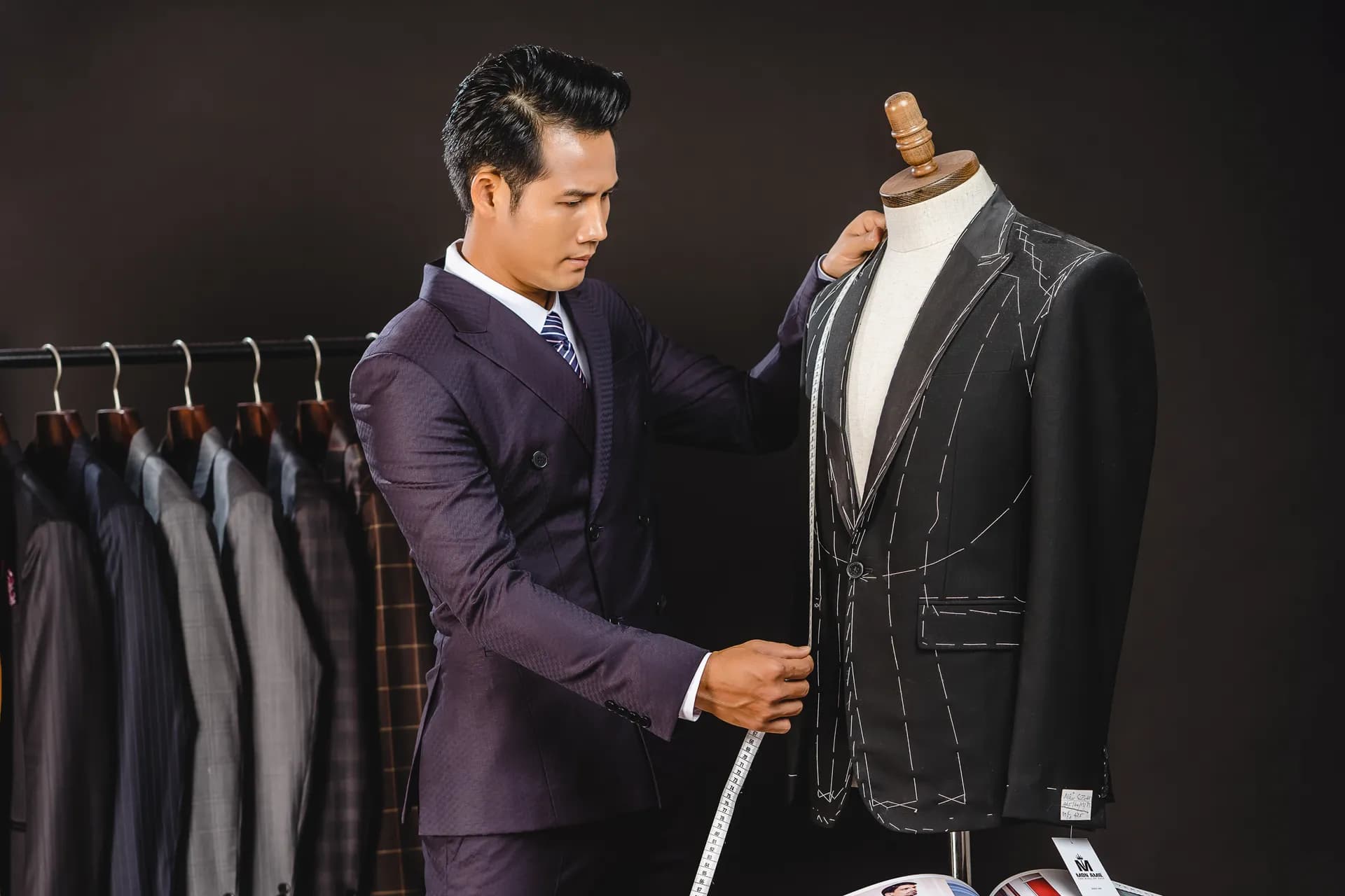 Người mẫu suit tím chỉnh áo vest phấn dựng trên manocanh, nền đen