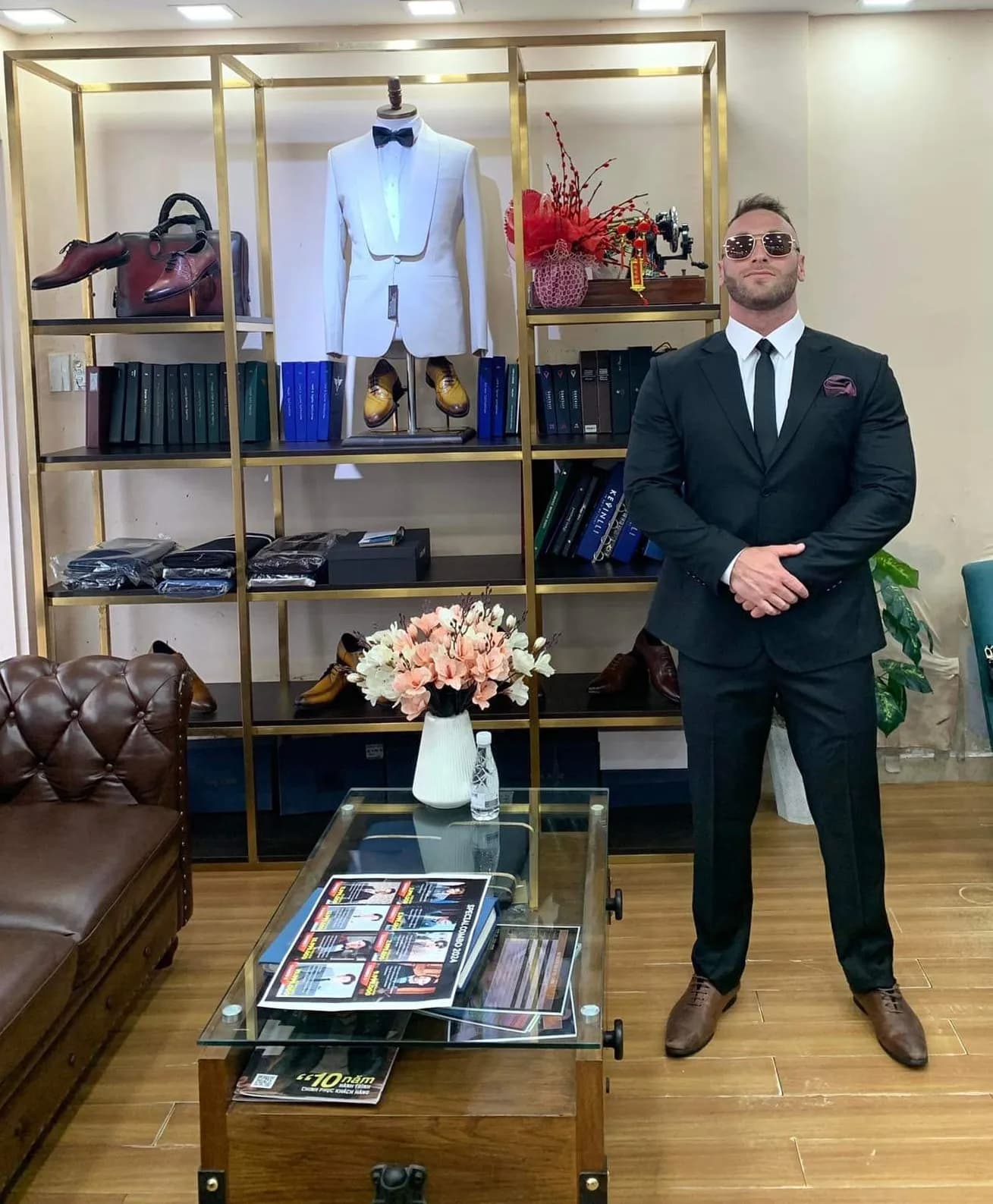 Suit đen cà vạt đen khăn túi đỏ, dáng đứng vững trước tủ trưng bày showroom
