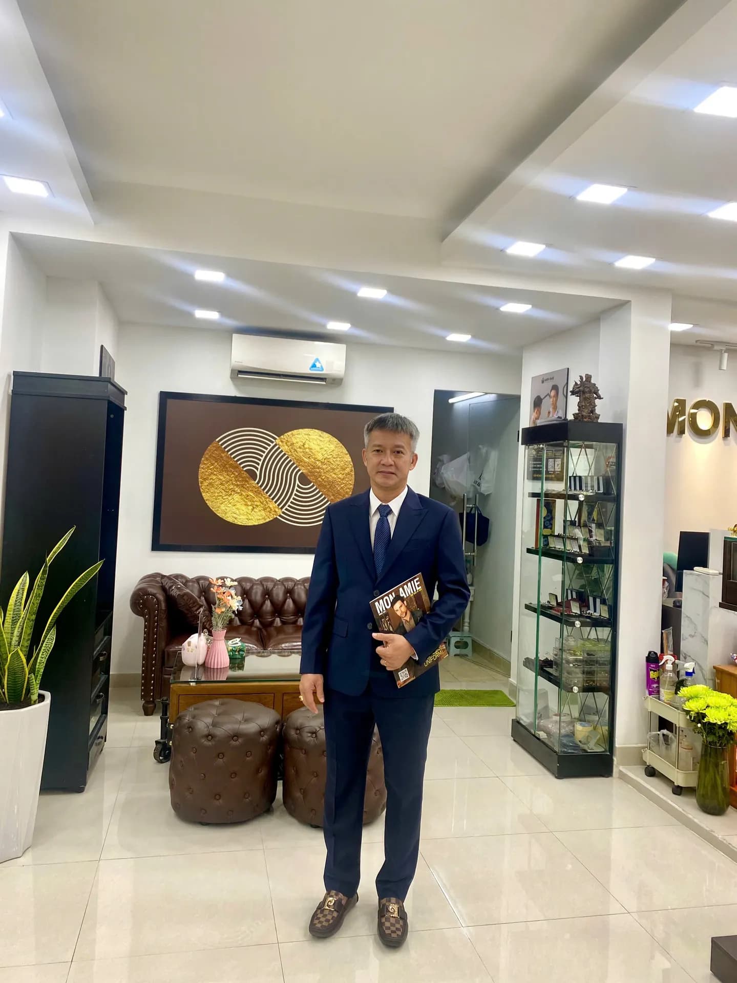 Suit navy cầm lookbook Mon Amie trong sảnh showroom sáng