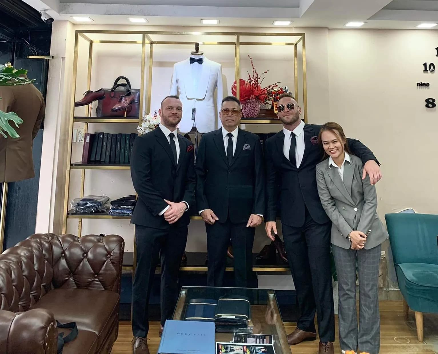 Ảnh tập thể bốn người trong suit đen và xám trước tủ tuxedo trắng