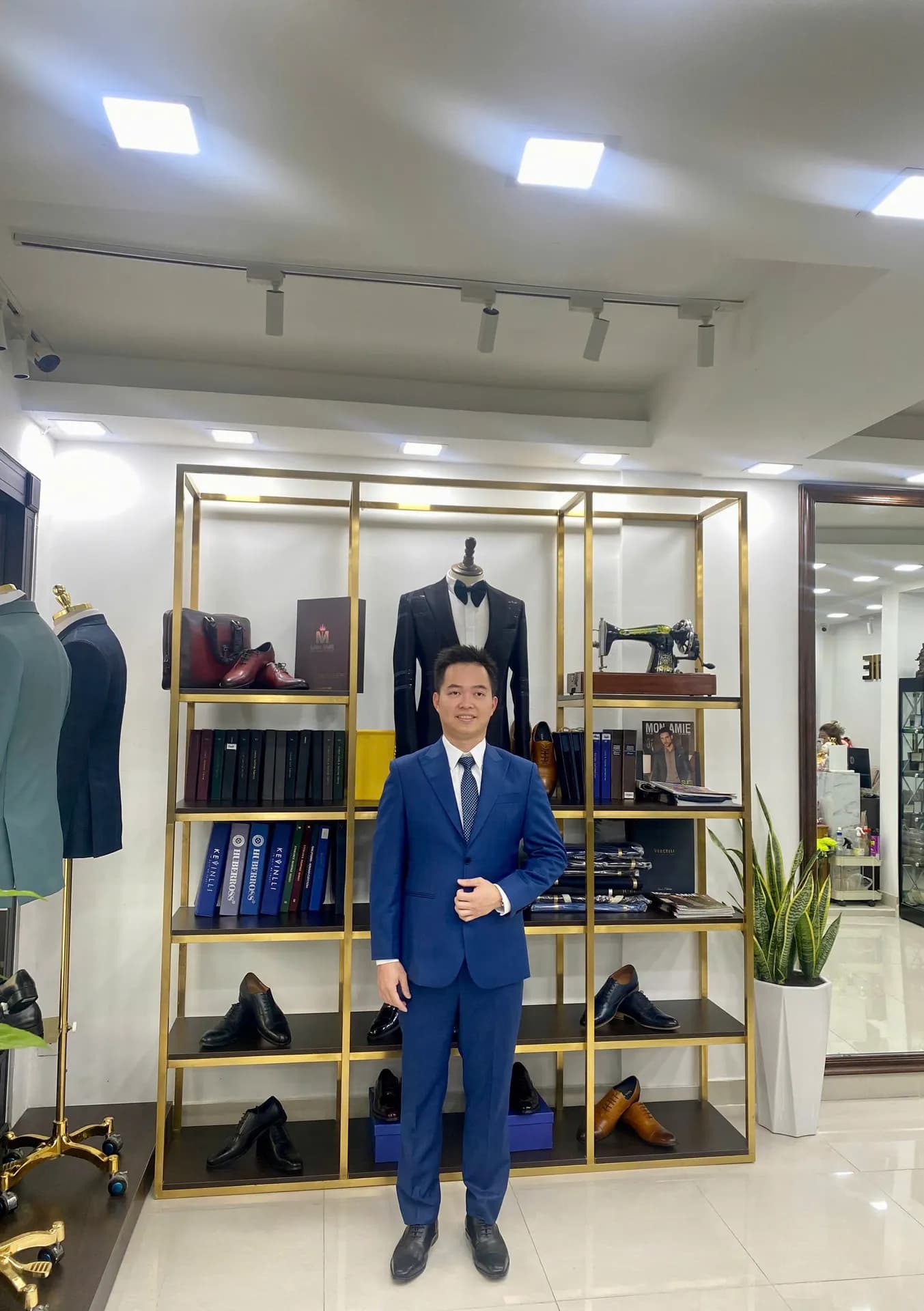 Suit xanh coban sáng, tay cài khuy, đứng trước kệ trưng bày