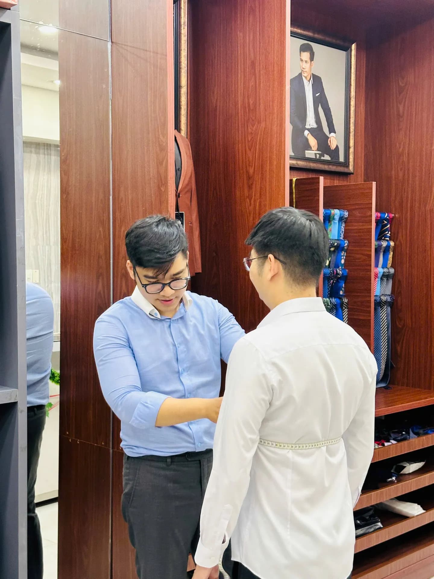 Nhân viên đo số đo cho khách mặc sơ mi trắng bên tủ gỗ