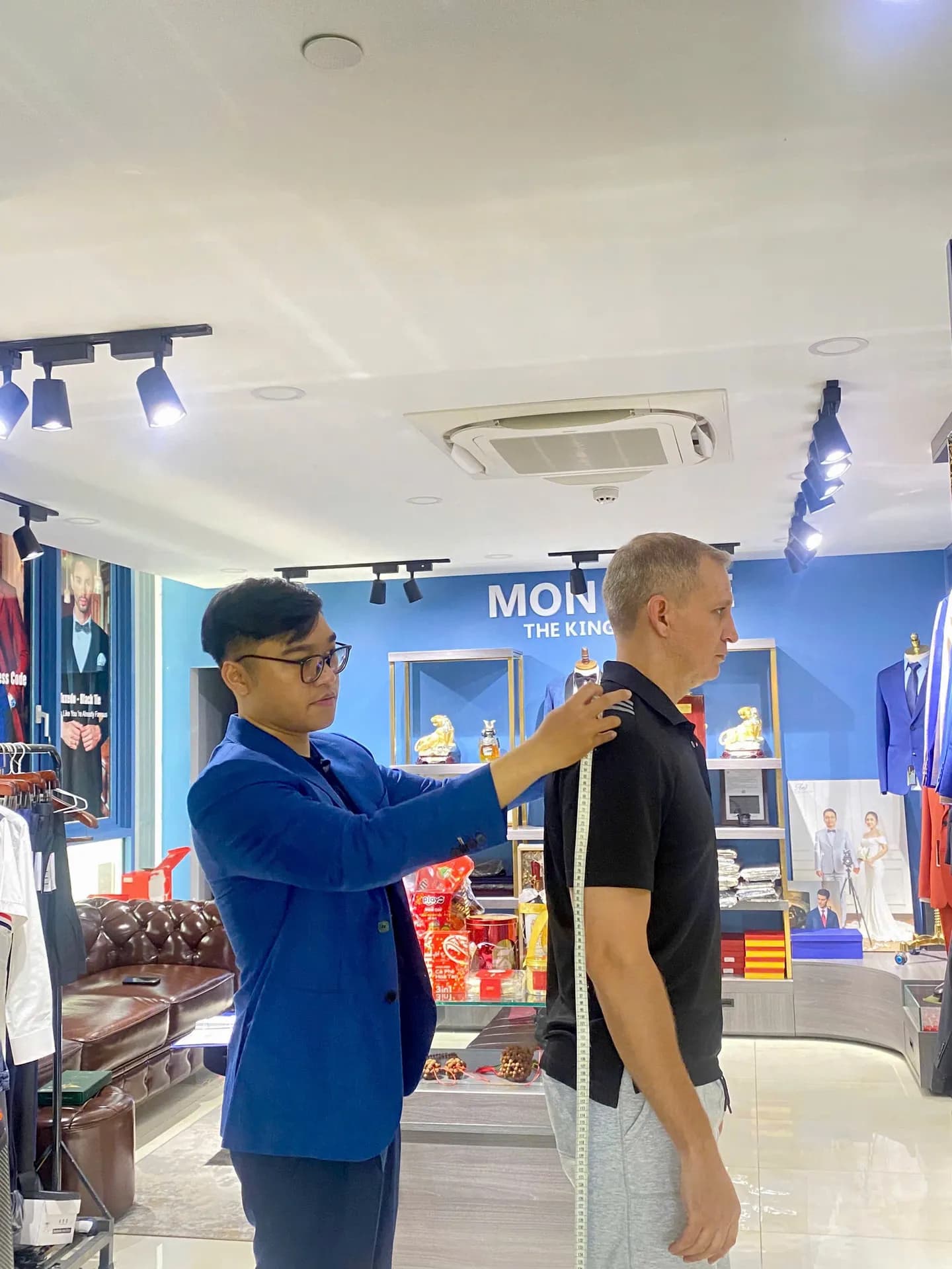 Nhân viên áo xanh đo vai cho khách tại showroom tường xanh