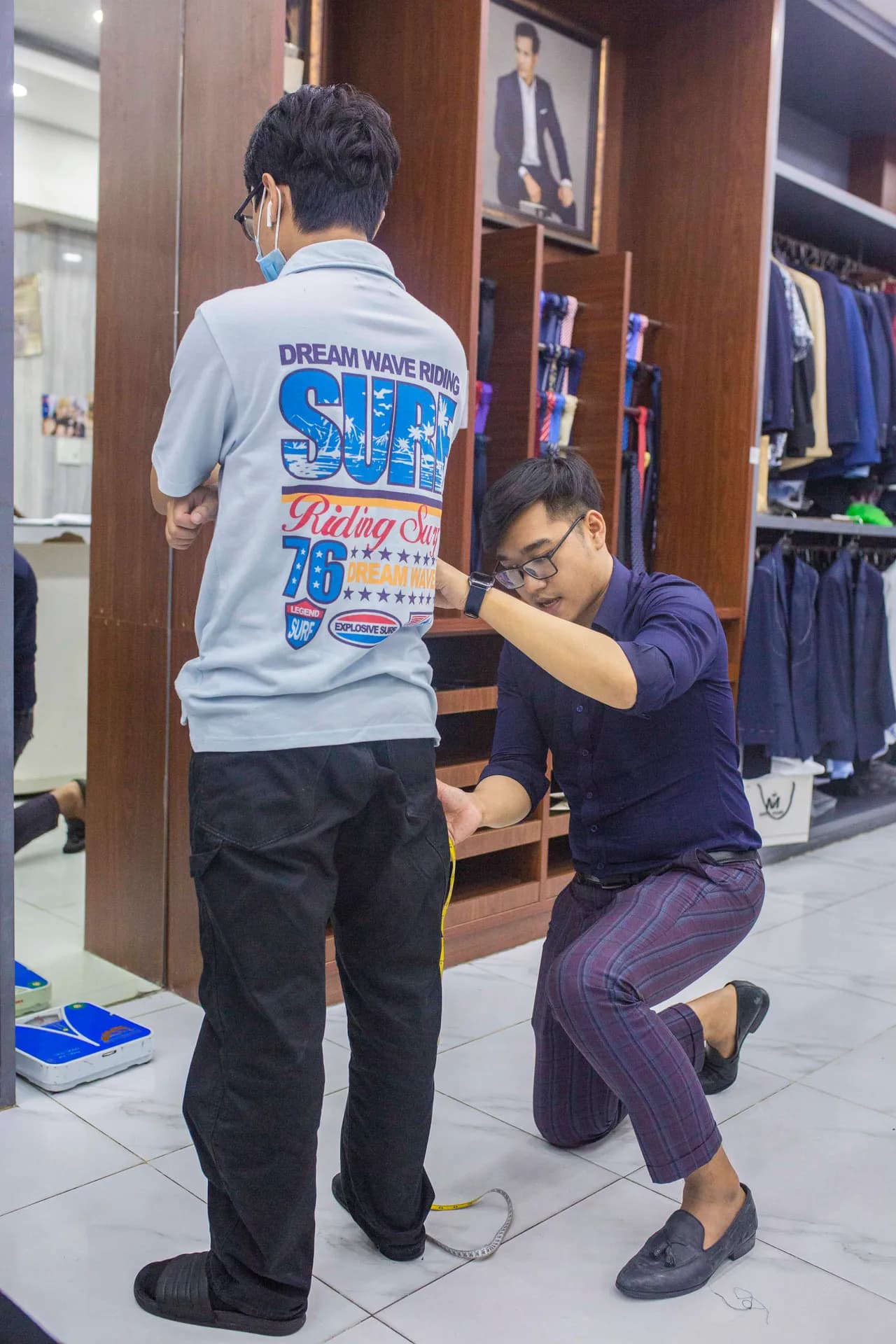 Thợ may quỳ đo chiều dài ống quần cho khách tại showroom