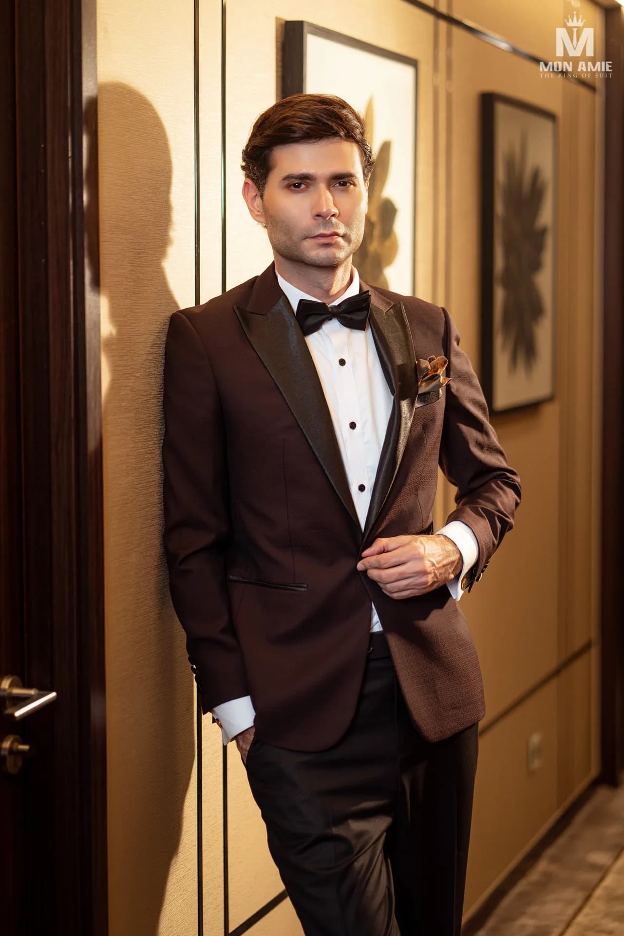Tuxedo nâu ve nhọn phối satin, sơ mi ngực xếp ly, dáng đứng tựa cửa.