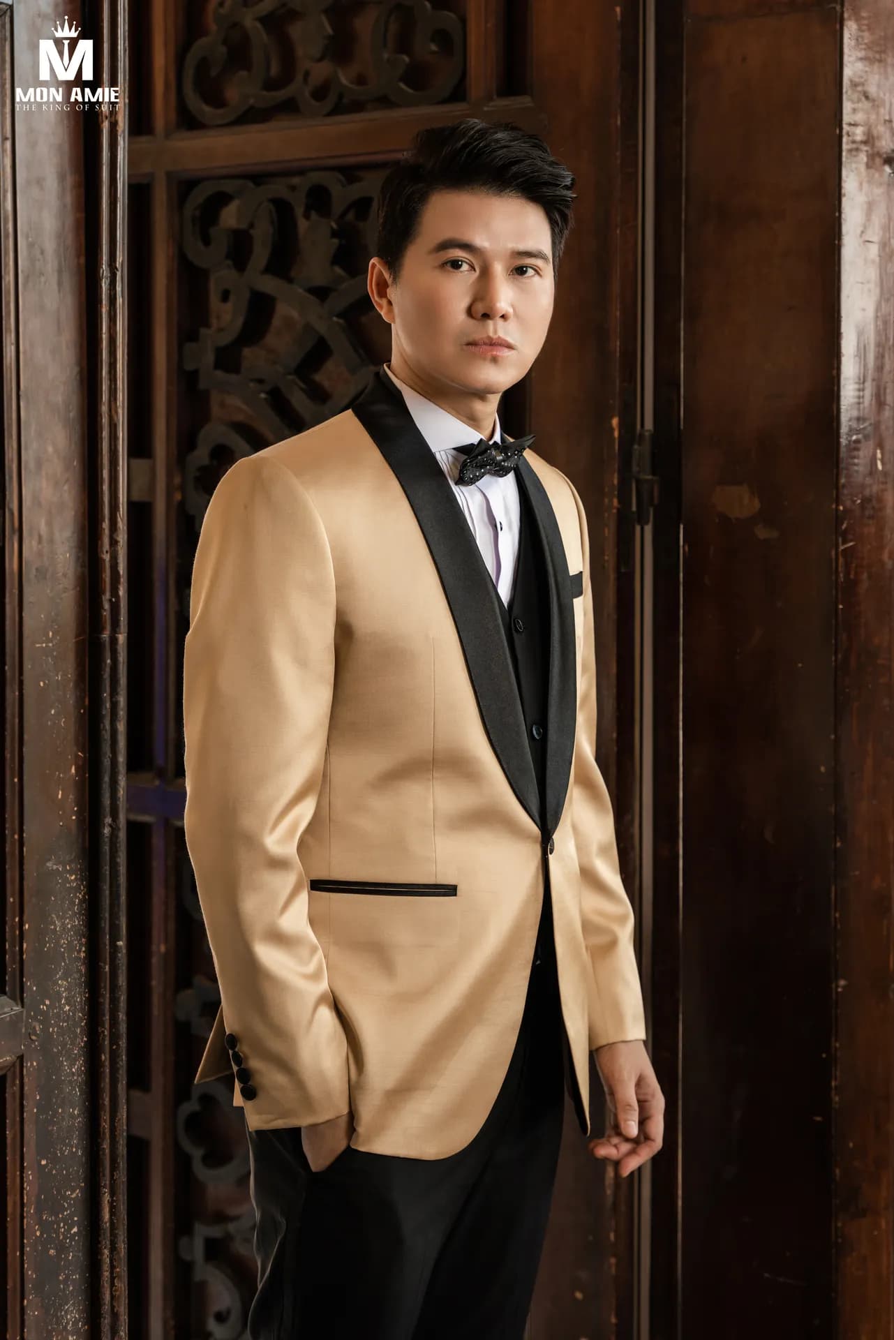 Vest vàng champagne cổ lụa đen trước cửa gỗ chạm khắc