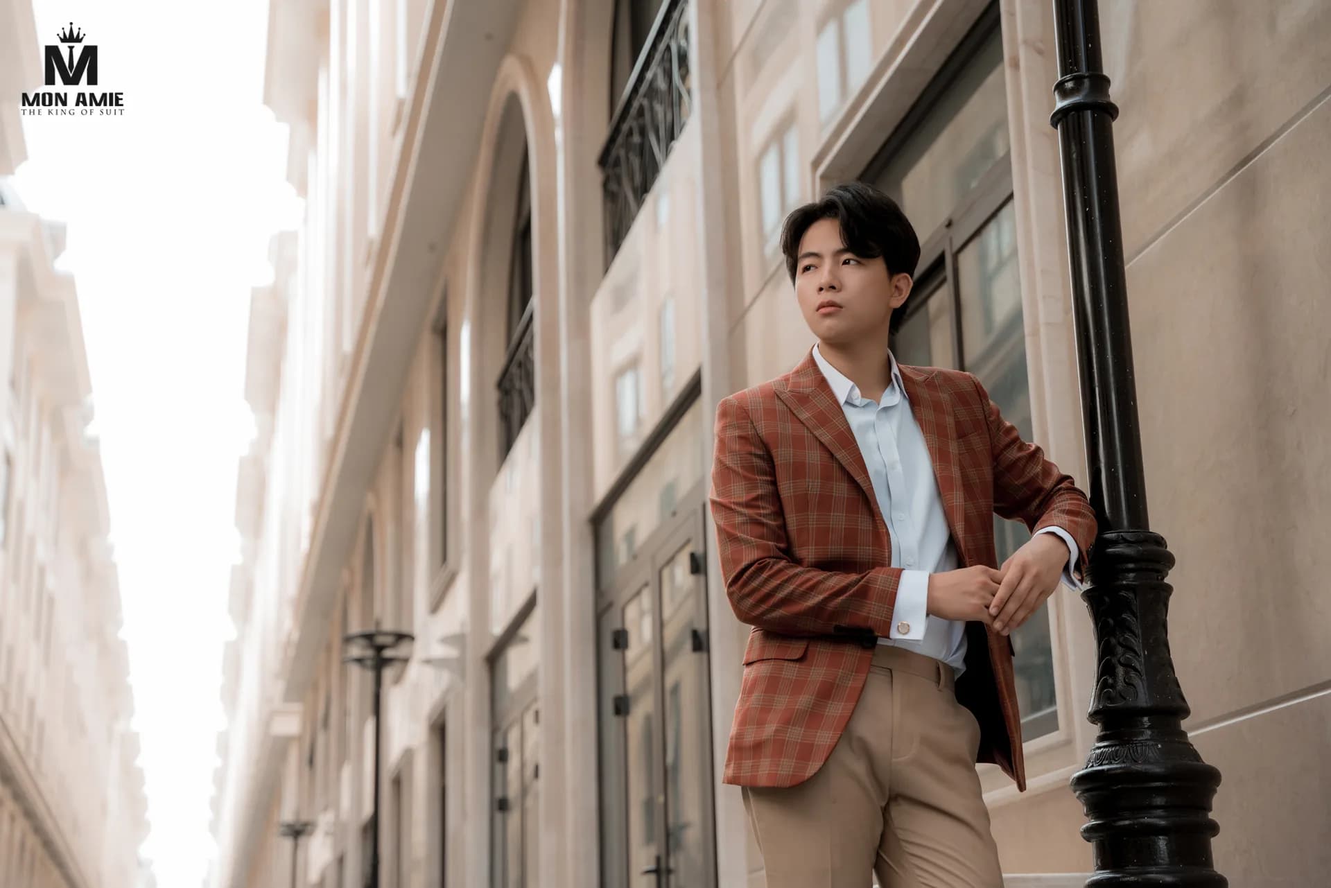 Blazer caro cam gạch, quần be, dựa cột đèn sắt trên phố kiến trúc Âu