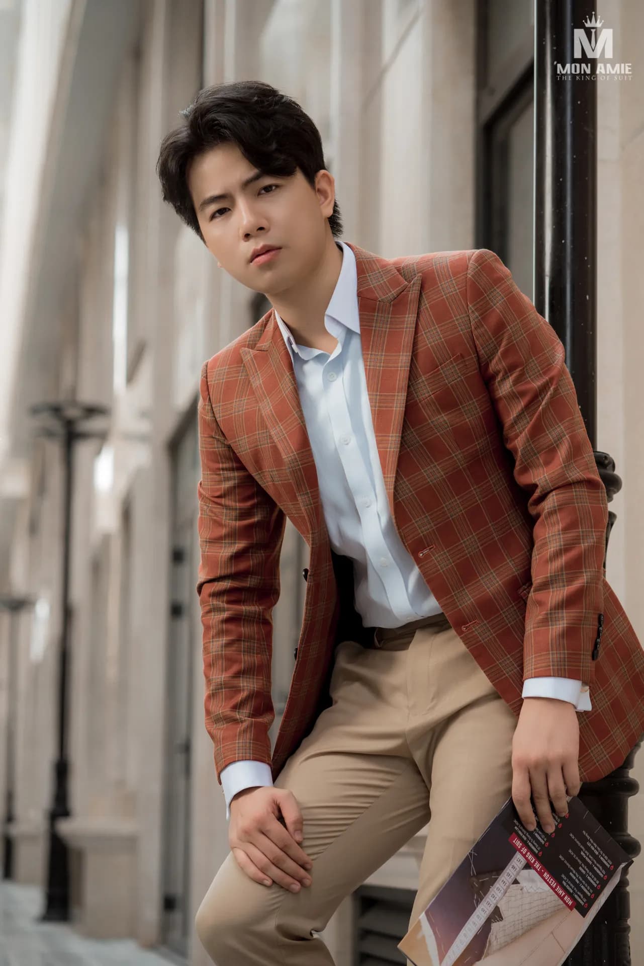 Blazer caro cam gạch, sơ mi xanh nhạt, ngồi tựa bậc đá, cận cảnh