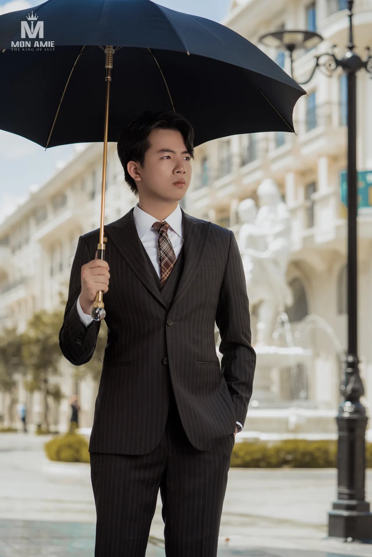 Suit nâu sọc ba mảnh, xòe ô đen, đứng giữa phố kiểu châu Âu