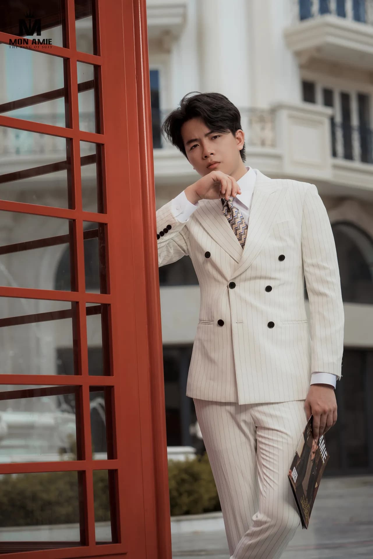 Suit trắng kem hai hàng khuy, nghiêng người bên buồng điện thoại đỏ, cận cảnh