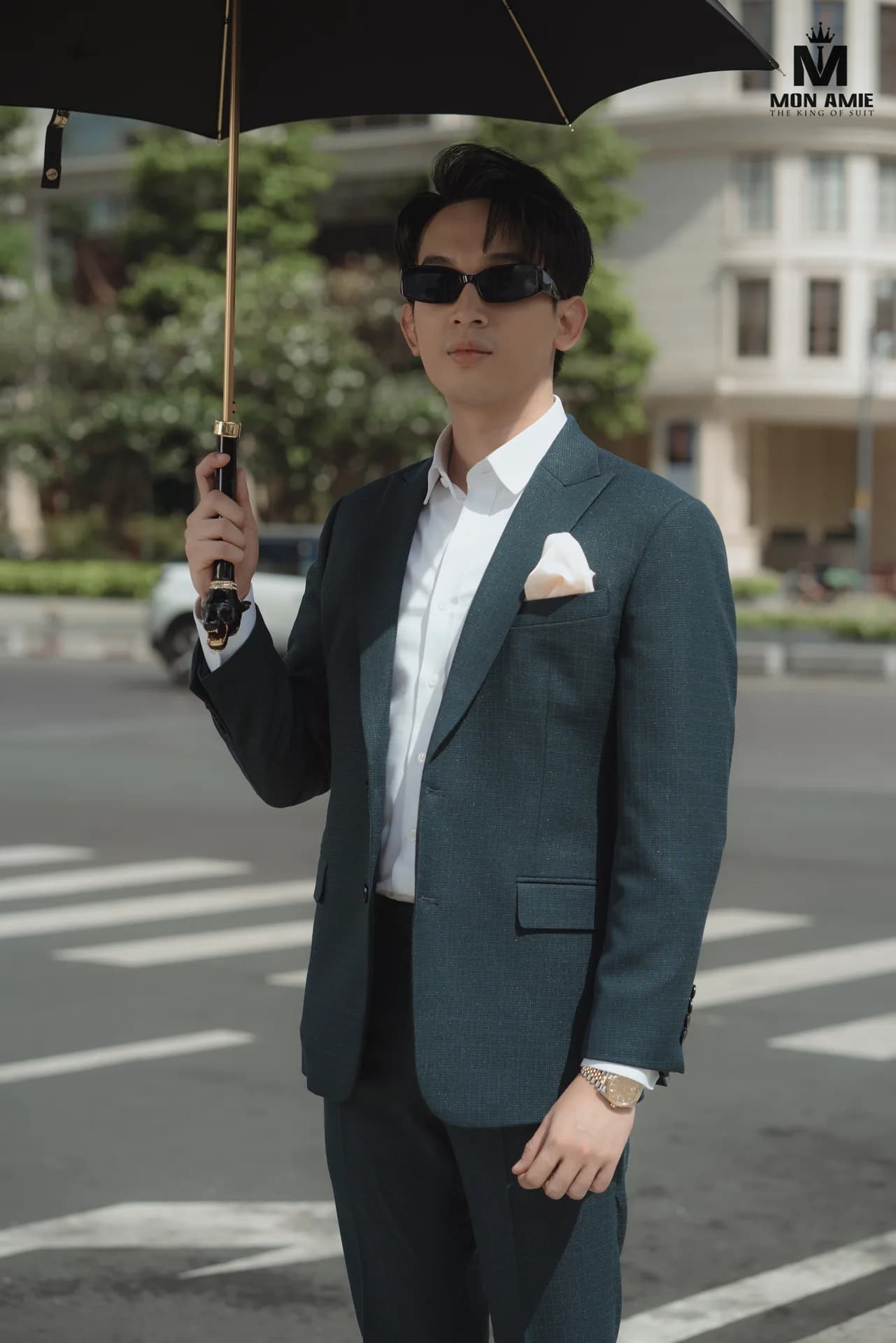 Suit xanh rêu, khăn túi trắng, cầm ô đen giữa ngã tư nắng đẹp