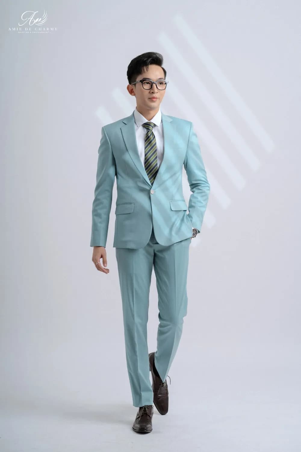 Suit xanh ngọc nhạt, cà vạt sọc, sải bước toàn thân trong studio sáng
