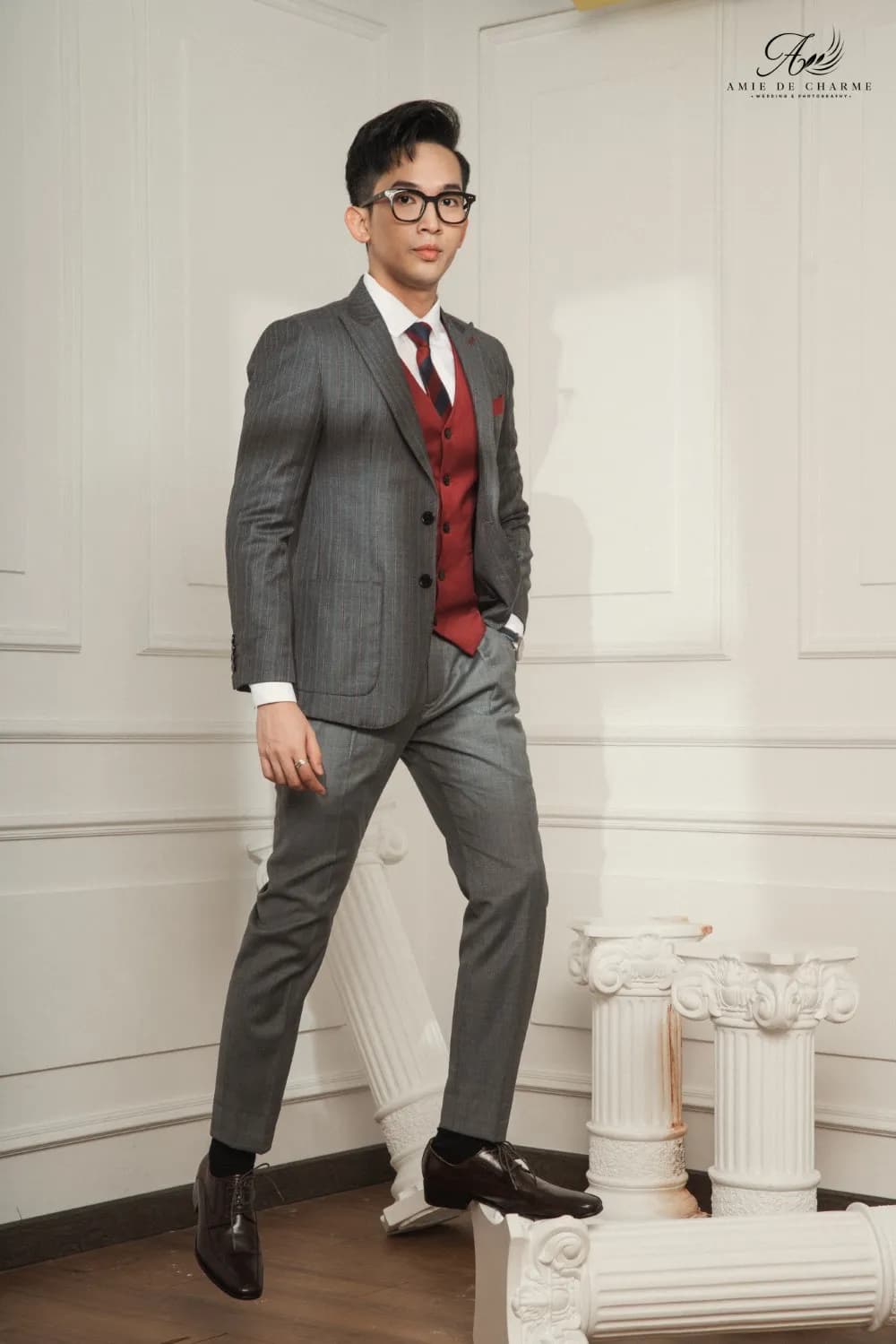 Suit xám kẻ sọc và gilê đỏ rượu, bước nhẹ giữa cột La Mã trắng