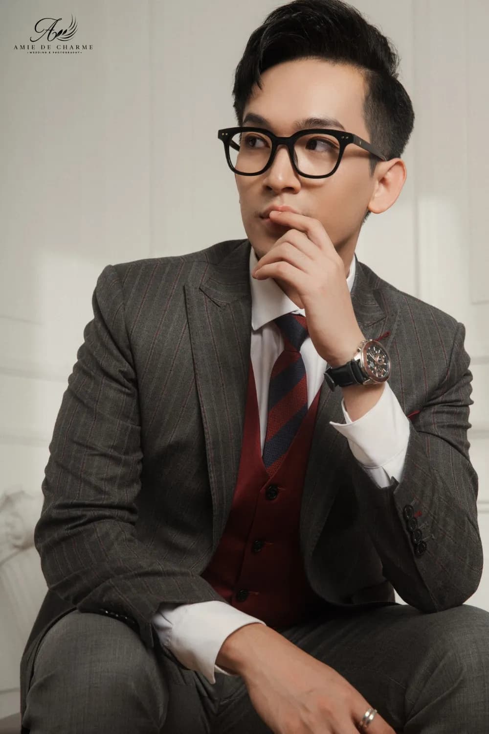 Suit xám gilê đỏ rượu, kính đen, tay chống cằm trầm tư