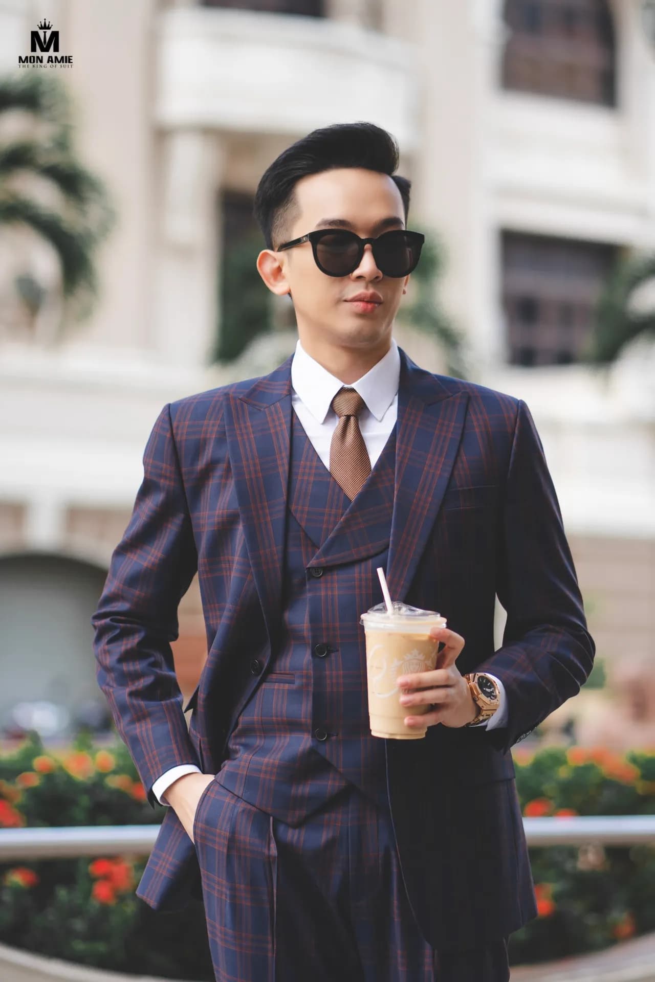 Suit ba mảnh kẻ caro tím, cầm ly cà phê, cận cảnh nền hoa đỏ