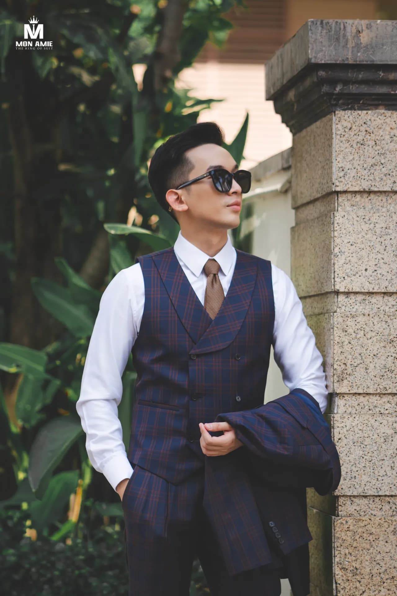 Gile xanh navy, sơ mi trắng, vắt áo vest qua vai, nền cây xanh