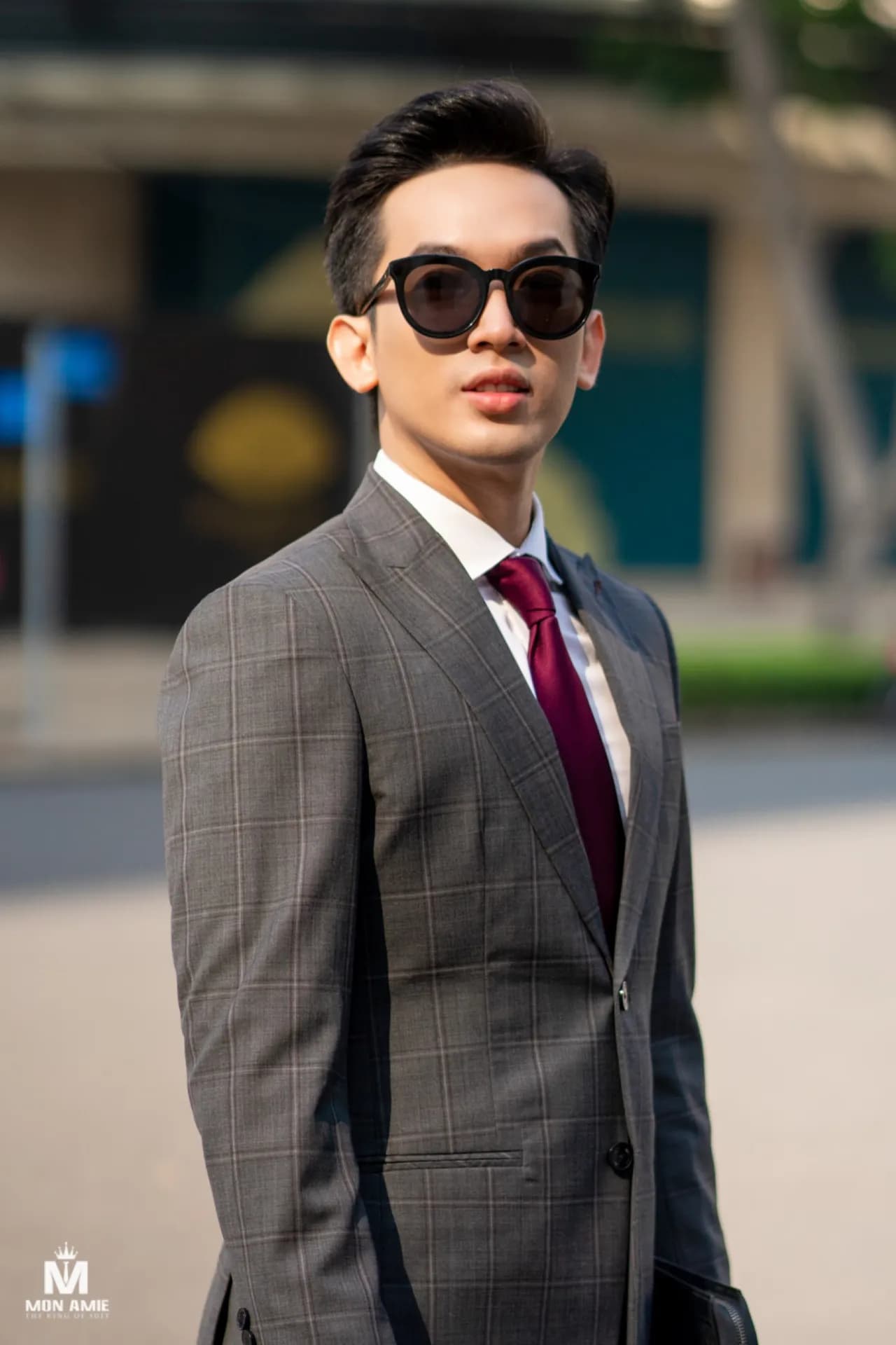 Suit xám nâu, cà vạt đỏ đô, kính râm, ngoảnh nhìn qua vai cận cảnh