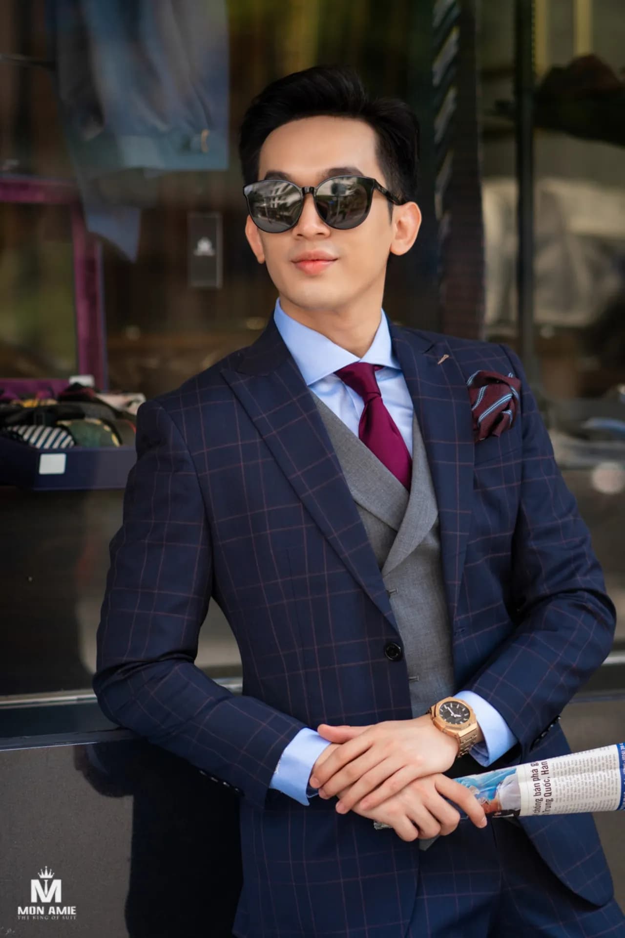 Suit ba mảnh caro xanh, gile xám, cà vạt đỏ đô, kính râm, tay khoanh