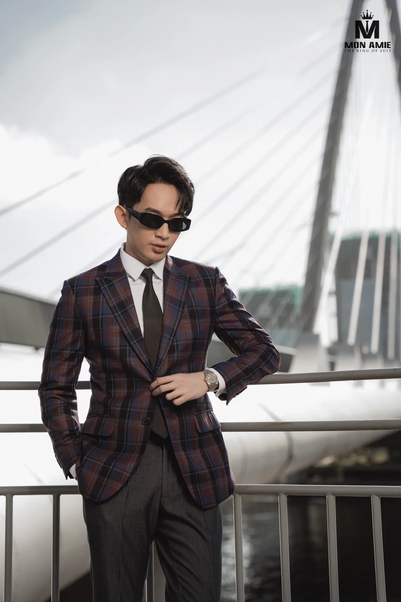 Blazer caro tím đô, kính râm, tay chống hông, nền cây cầu trắng