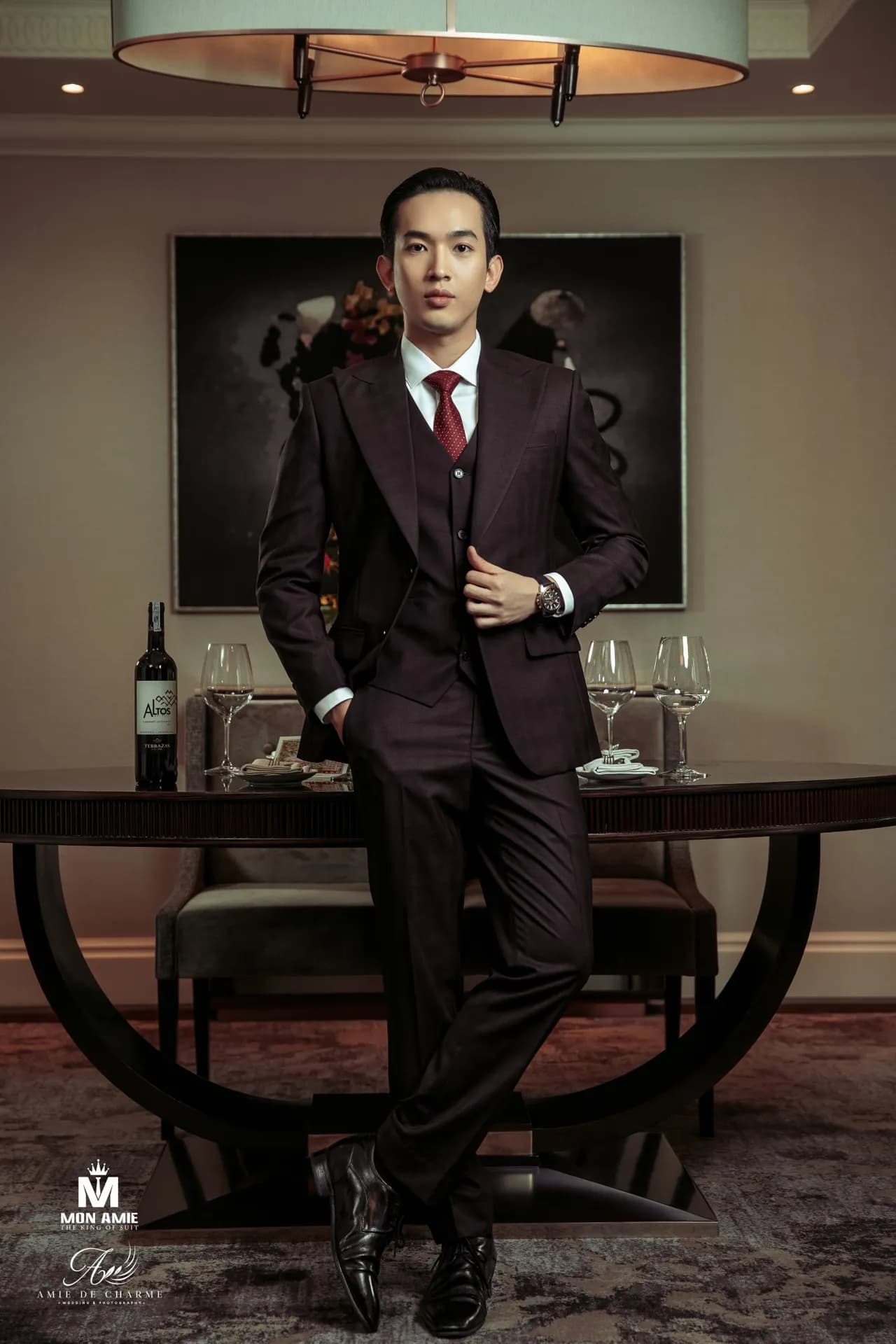 Suit ba mảnh nâu đen, dáng dựa thoải mái tay đút túi trong phòng ăn sang trọng