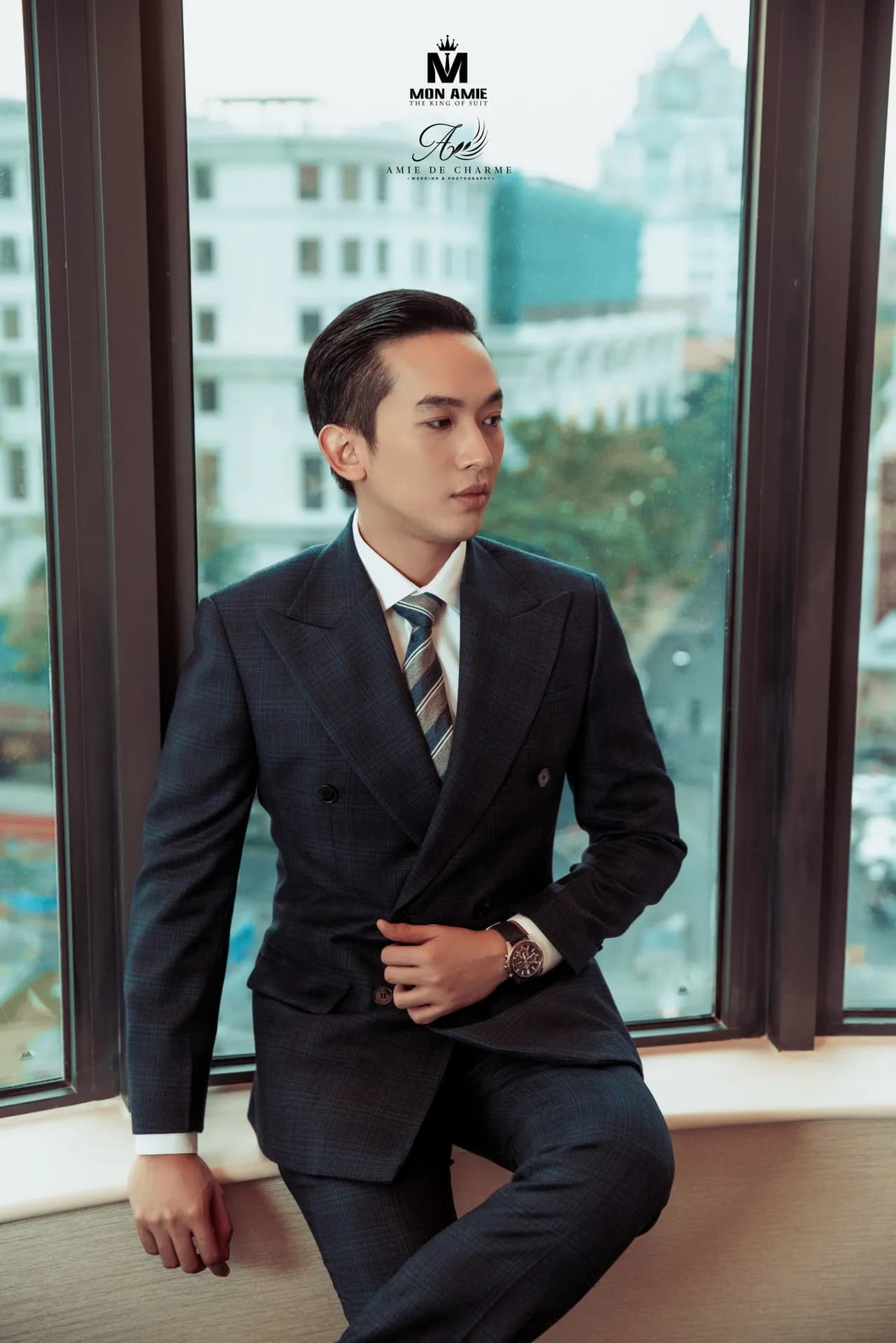 Suit navy cài hai hàng, ngồi tựa bệ cửa sổ, tay chỉnh áo, nhìn nghiêng